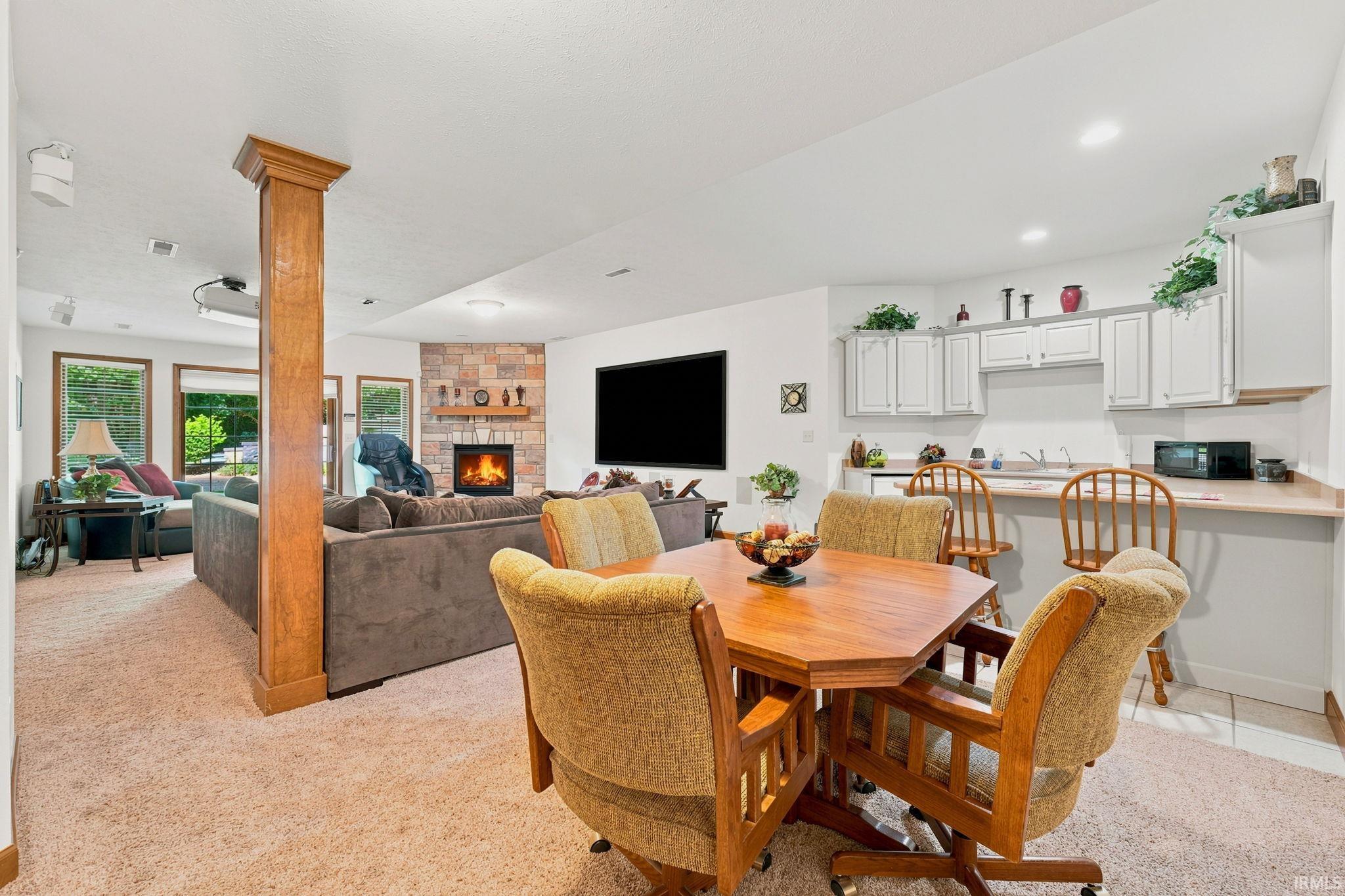 Open-concept living space featuring a stone-faced fireplace, a built-in wet bar with white cabinetry, and recessed lighting