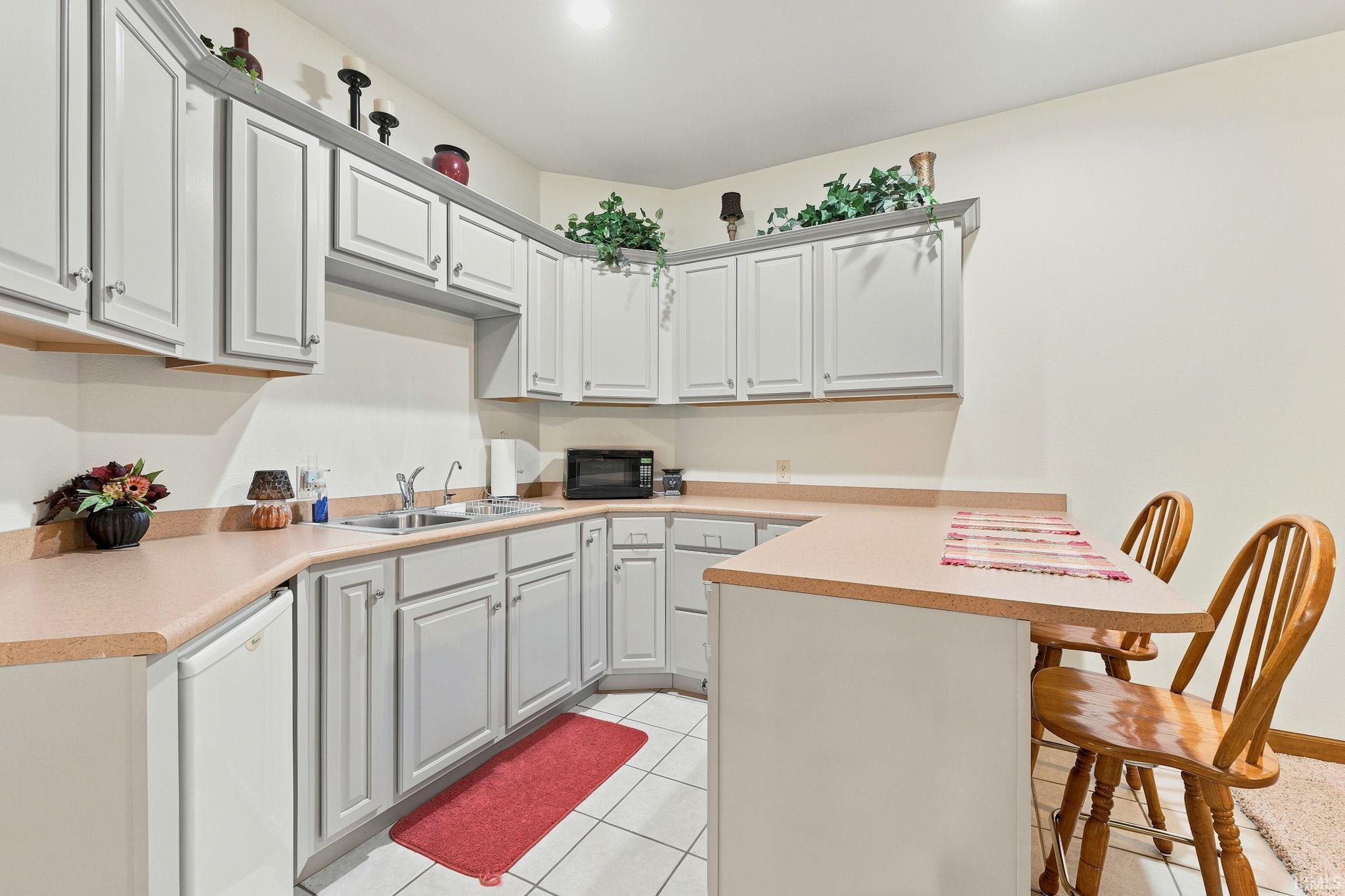 Kitchenette featuring light-toned cabinetry, a double basin sink, and a built-in breakfast bar with seating