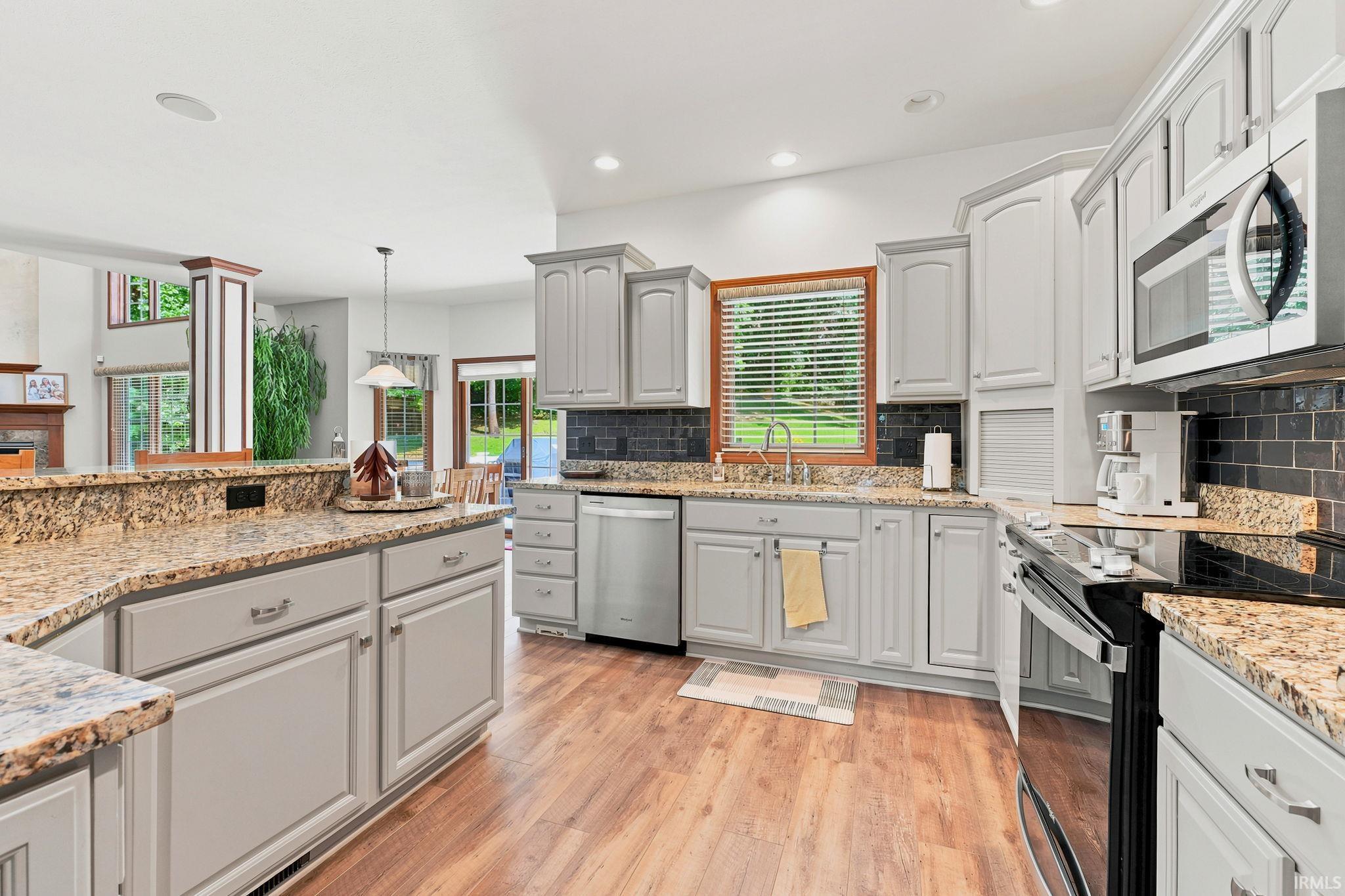 Kitchen featuring light-toned cabinetry, granite countertops, wood-finish flooring, stainless steel appliances, and a dark subway tile backsplash