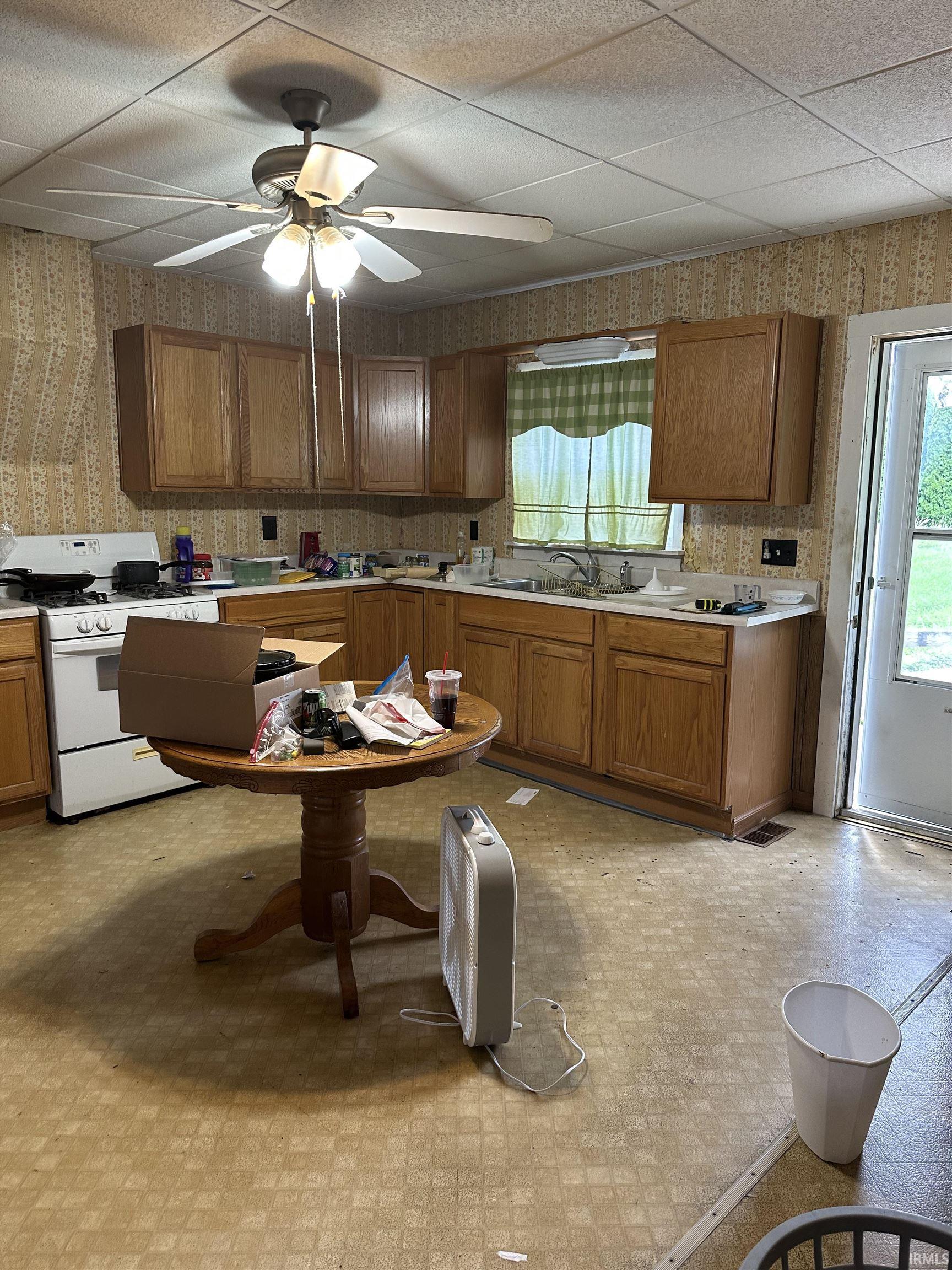 Kitchen featuring wood cabinetry, white appliances, a ceiling fan with integrated lighting, a window over the sink, and exterior access
