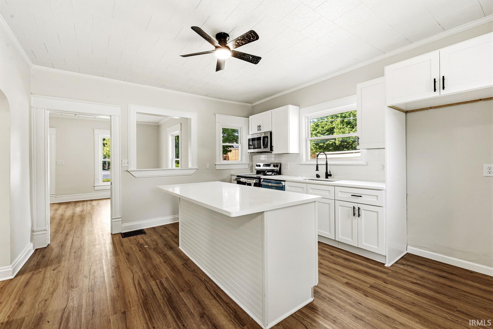 Modern kitchen featuring a central island with a solid surface countertop, white shaker cabinetry, wood-finish flooring, and a stainless steel appliance suite