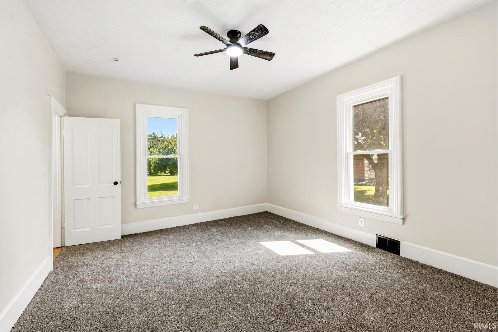 Spacious room featuring neutral paint, gray carpeting, a ceiling fan with integrated lighting, and white trim