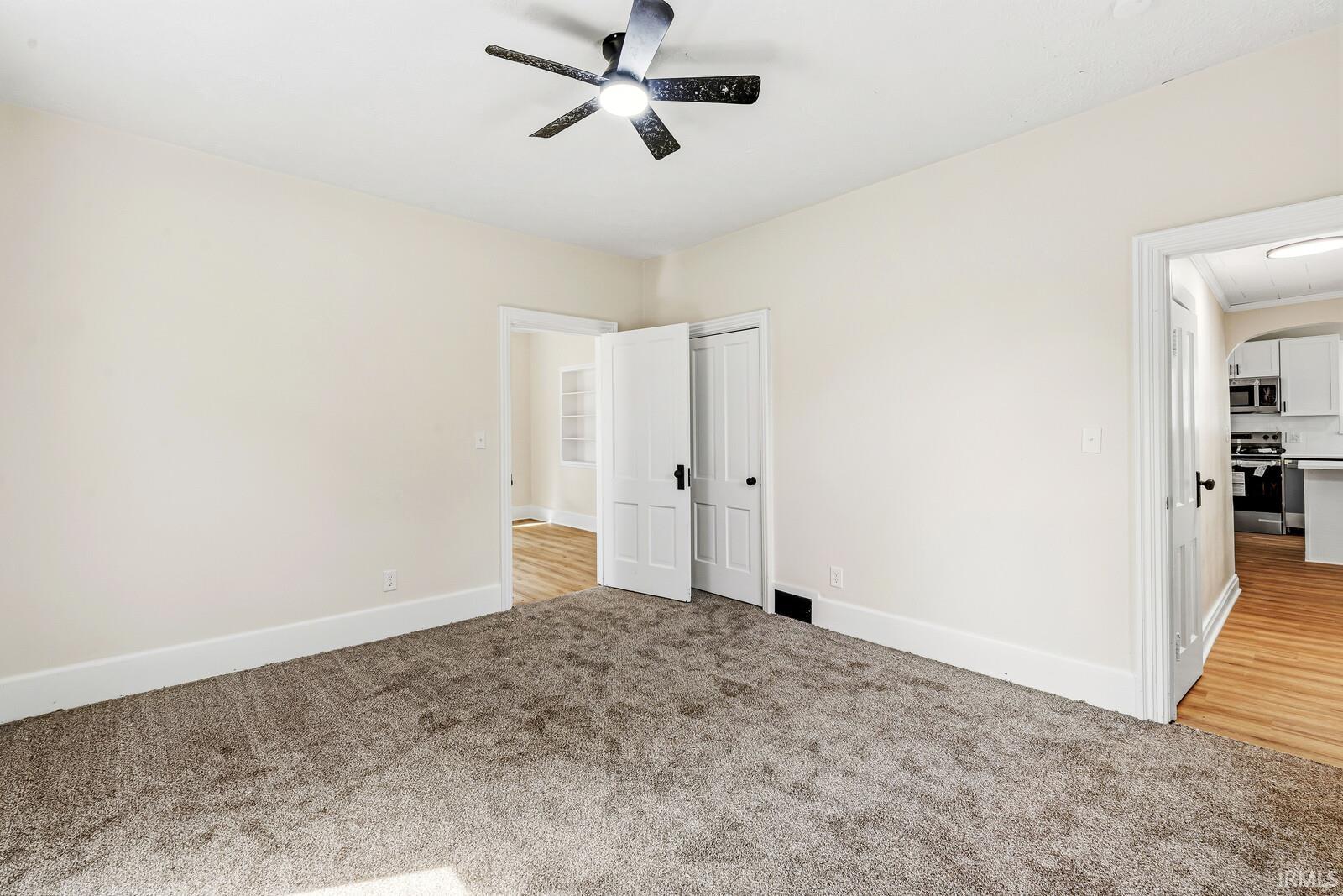 Carpeted interior space with a ceiling fan light fixture, white trim, and doors with dark hardware