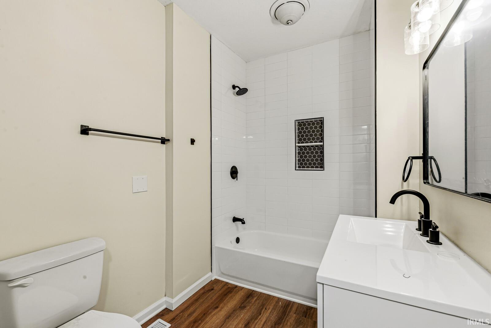 Contemporary bathroom featuring a white vanity with integrated sink, black fixtures, and a tiled shower-tub combination with an accent niche