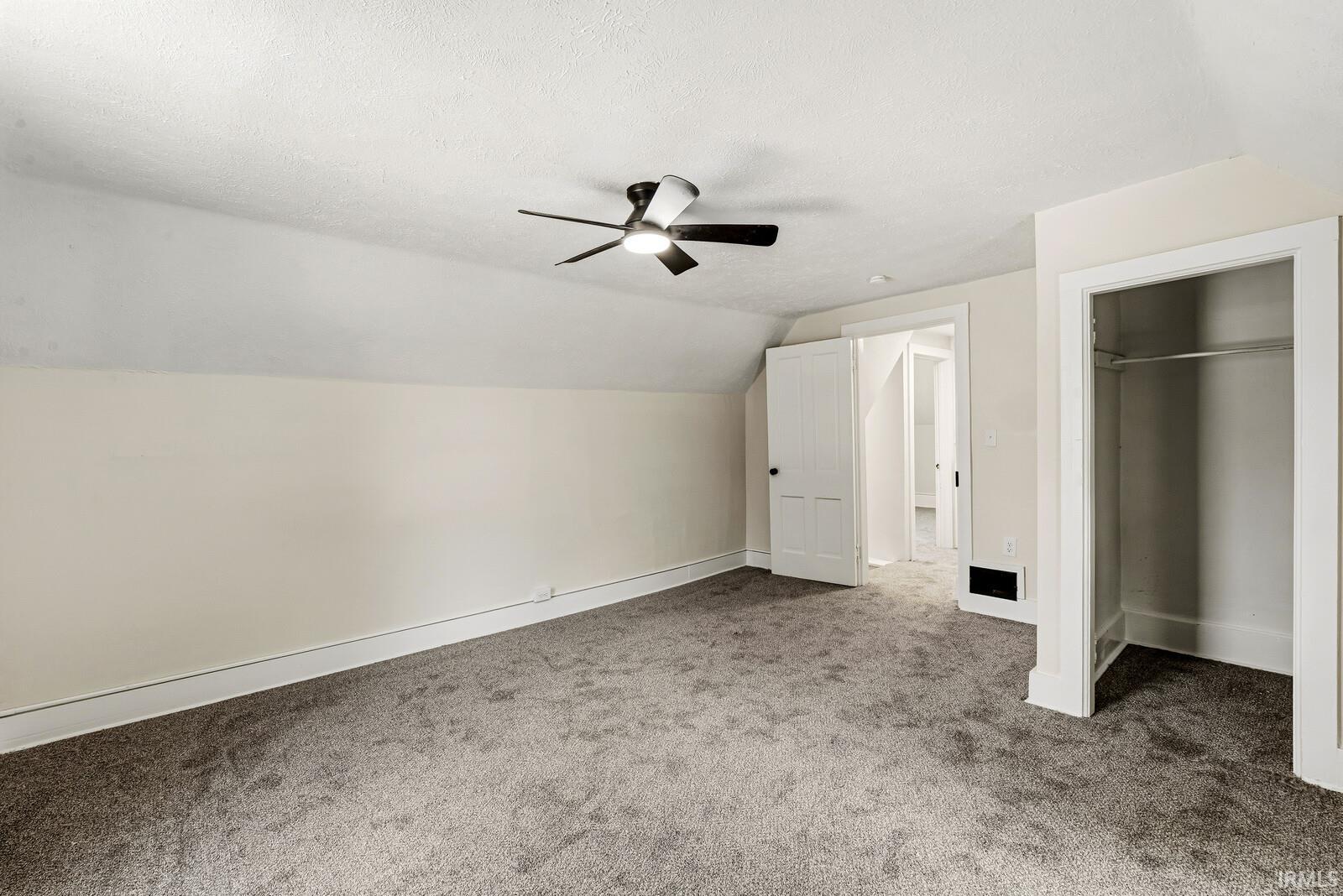 Spacious room featuring sloped ceilings, plush gray carpeting, a contemporary ceiling fan, and crisp white trim