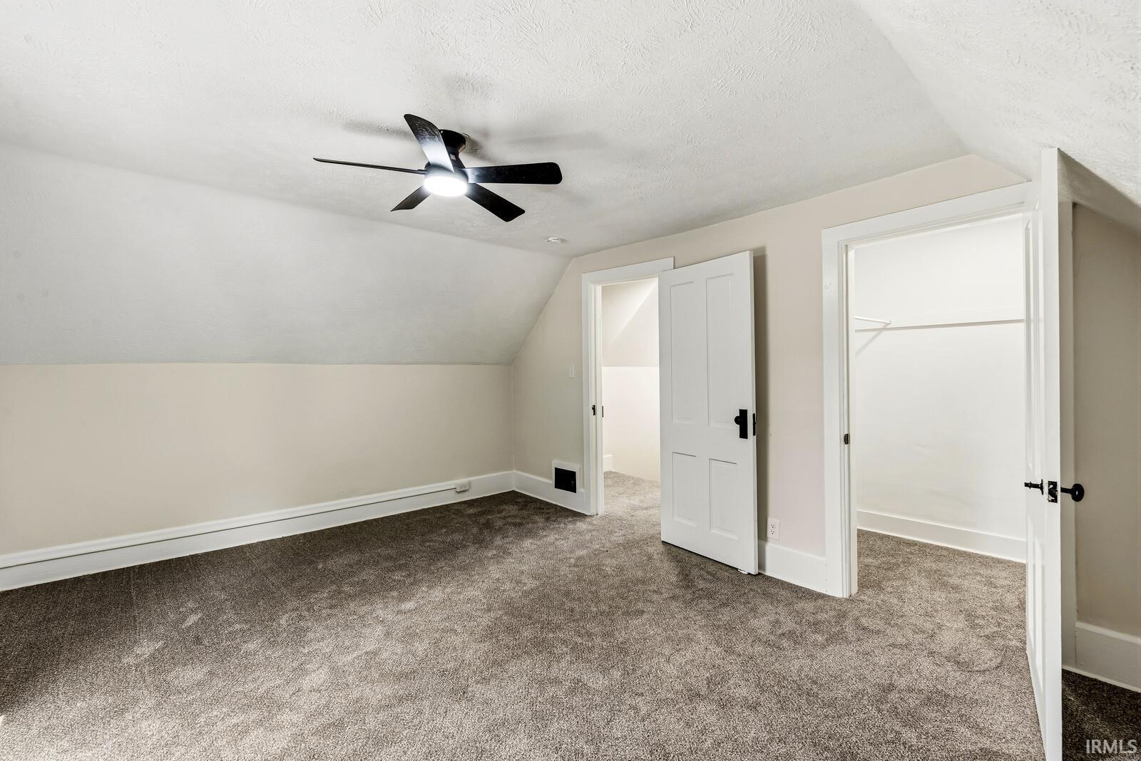 Carpeted room featuring a ceiling fan with integrated lighting, a sloped ceiling, multiple interior doors, and a built-in closet with shelving