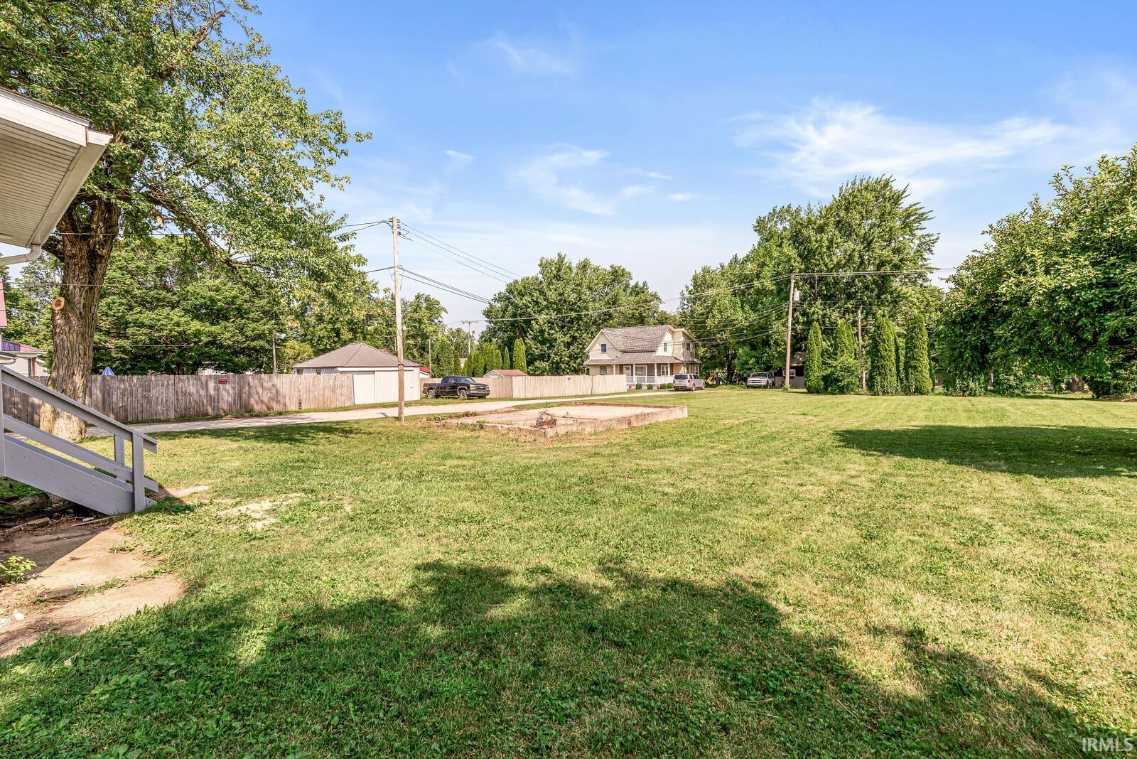 Expansive grassy lawn with mature trees and a partial wooden fence