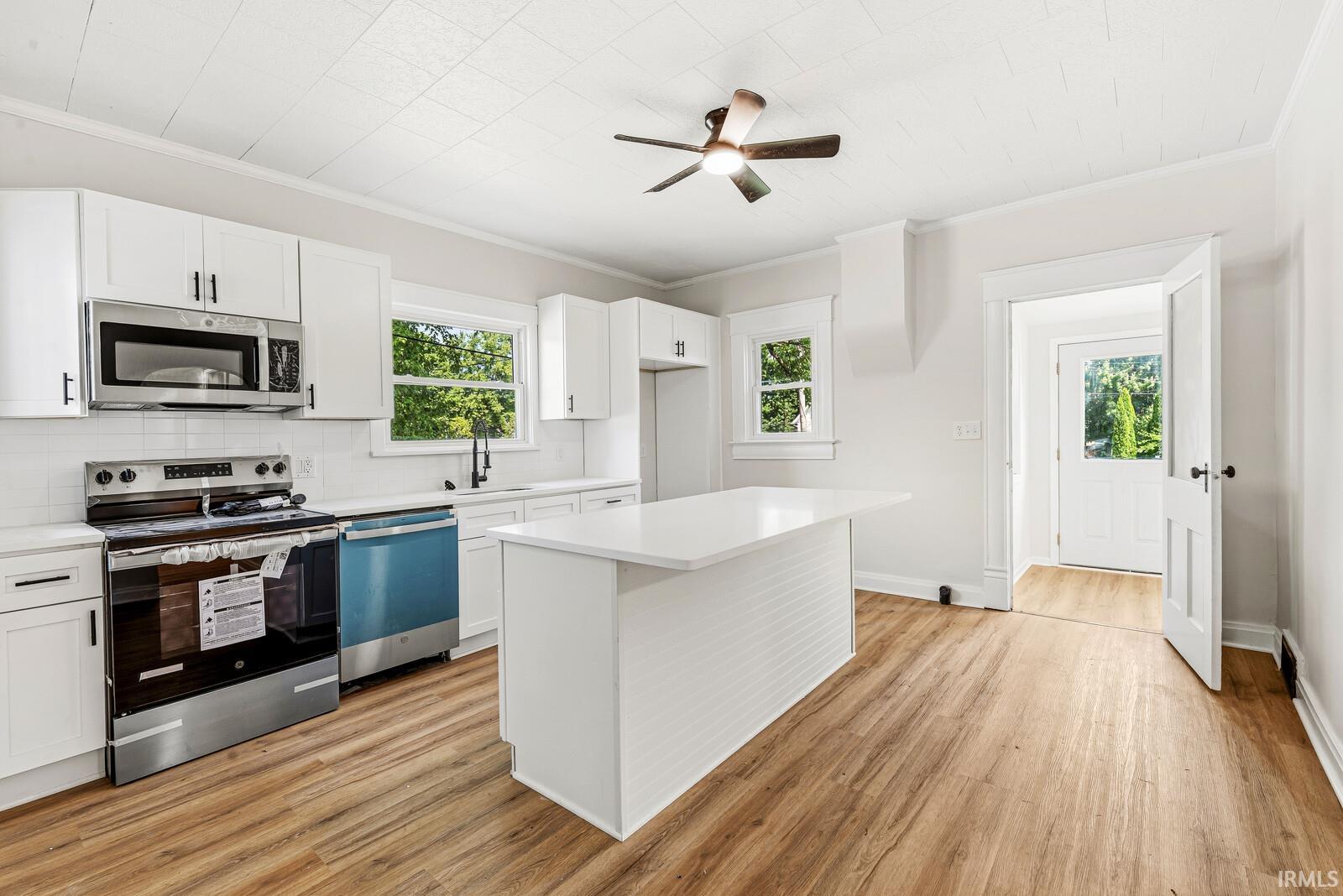 Contemporary kitchen featuring white cabinetry with dark hardware, stainless steel appliances, a center island with a white countertop, and wood-finish flooring