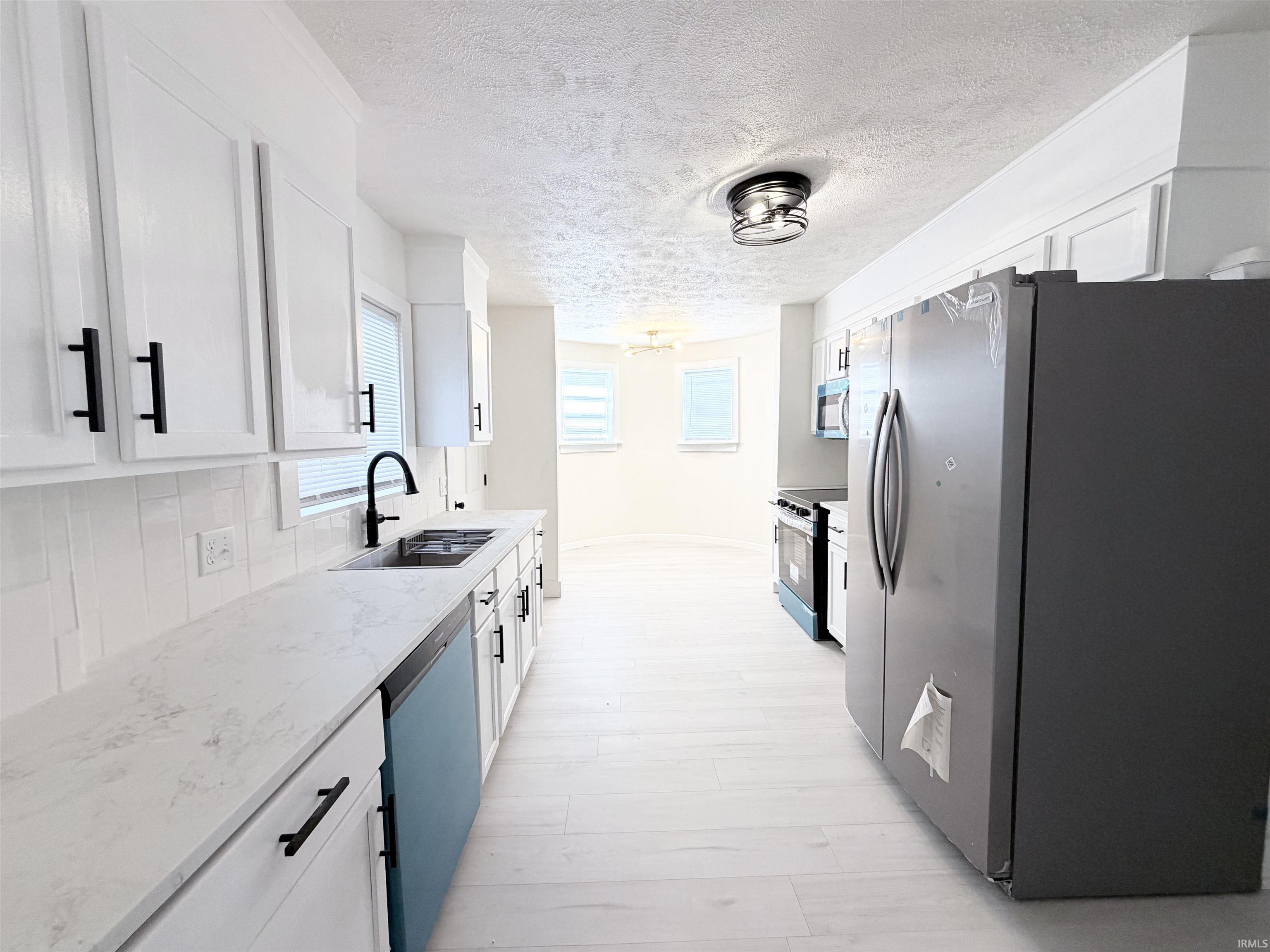 Modern kitchen featuring white shaker cabinetry with matte black hardware, light-toned countertops, and a subway tile backsplash