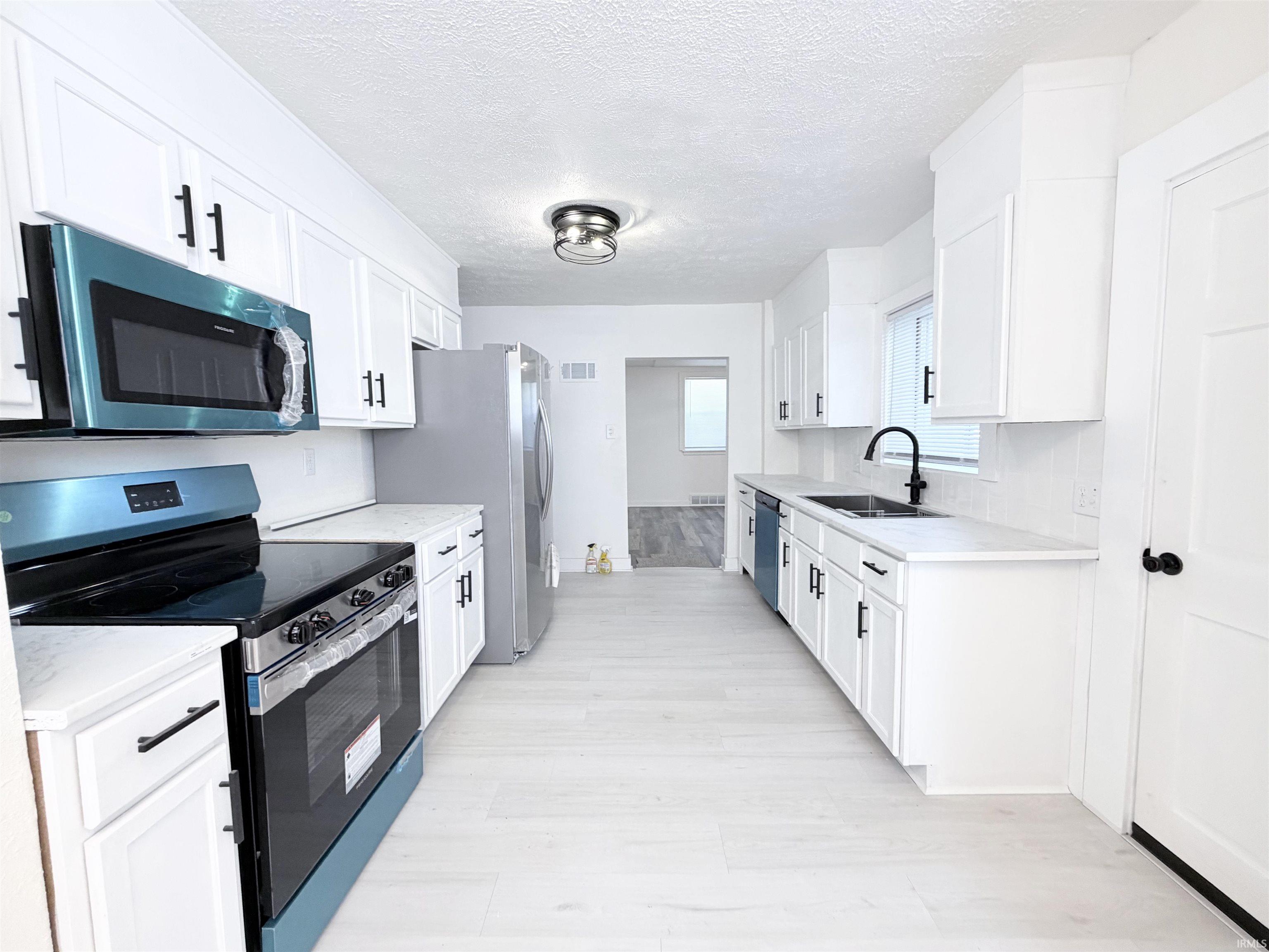 Contemporary kitchen featuring white cabinetry, light-toned wood-finish flooring, and white countertops