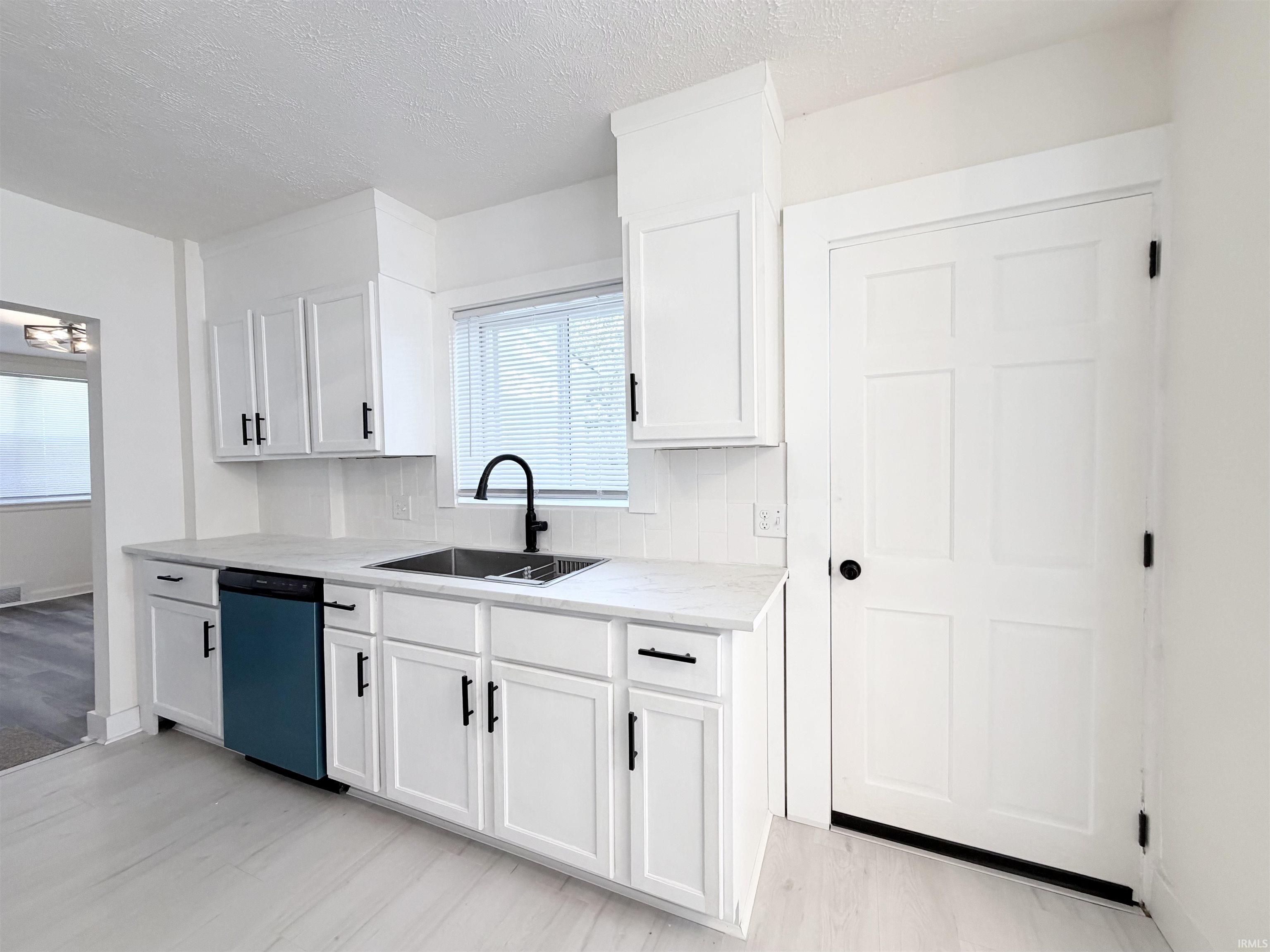 Kitchen featuring white shaker cabinetry, light-toned countertops, a matte black faucet, and a panel-front dishwasher