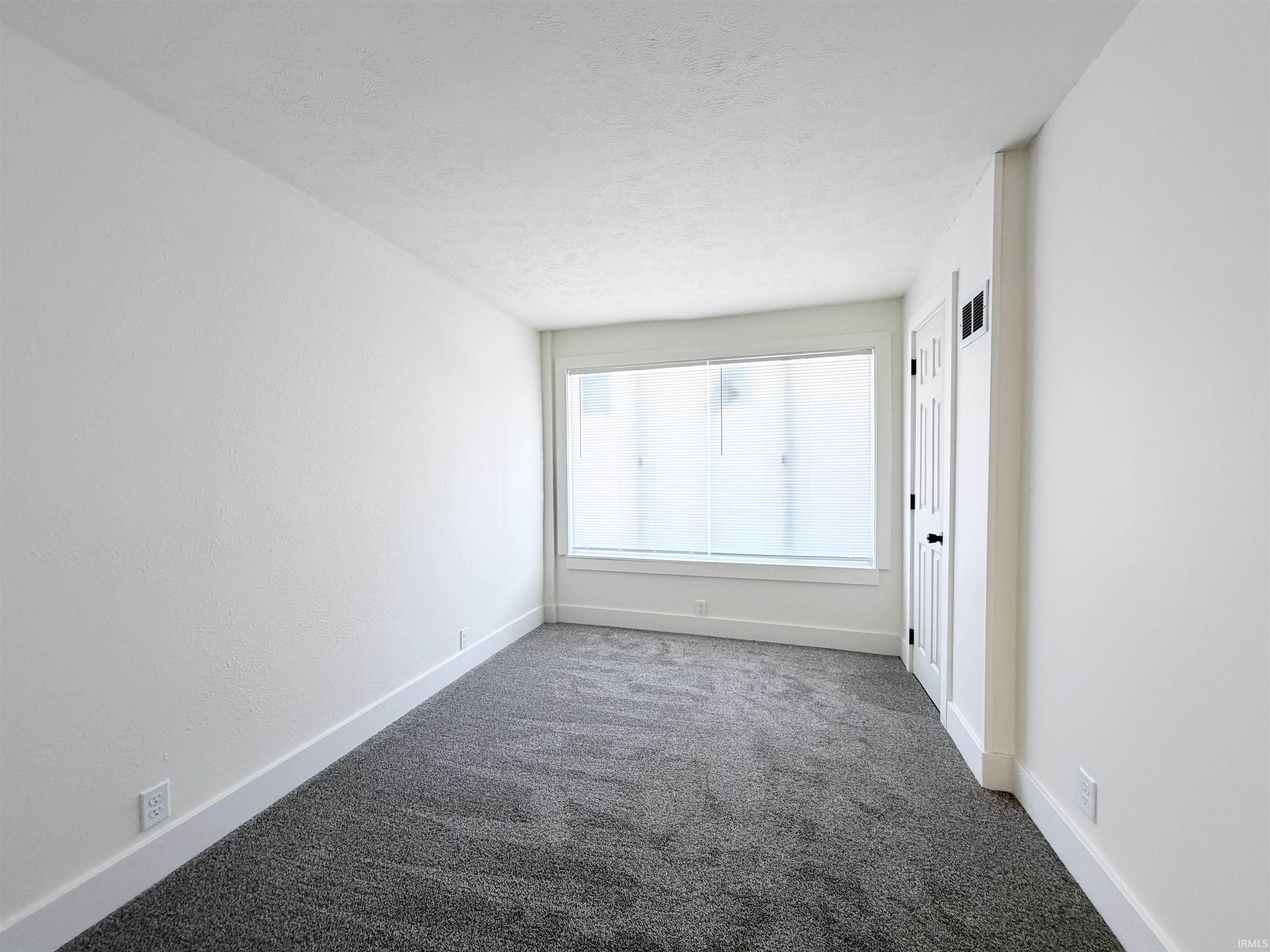 Carpeted room featuring a white door with black hardware, white baseboards, and a window with blinds