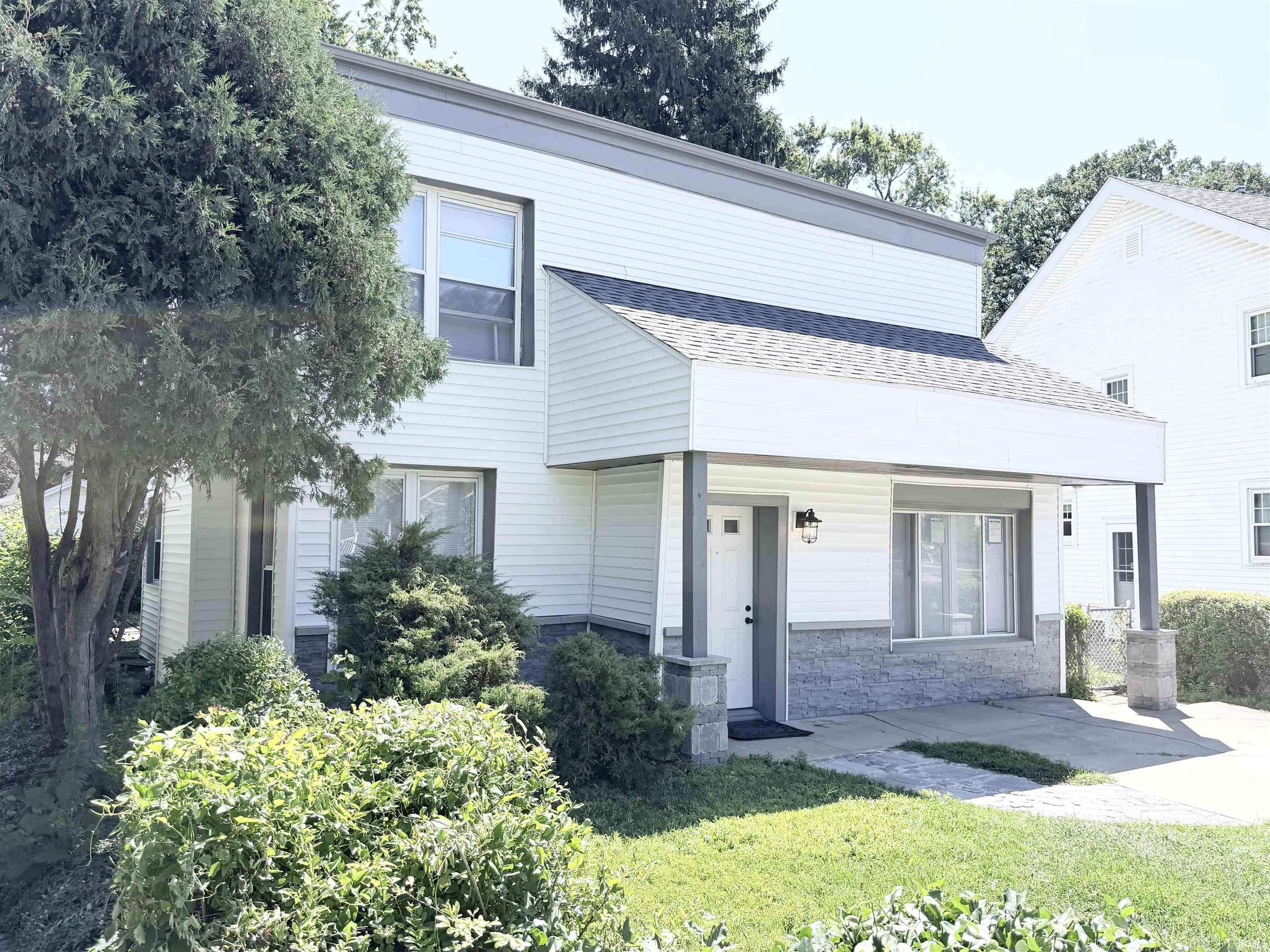 Two-story residence featuring white siding, a covered front porch with gray support columns, a dark gray roof, and a gray stone-finish foundation