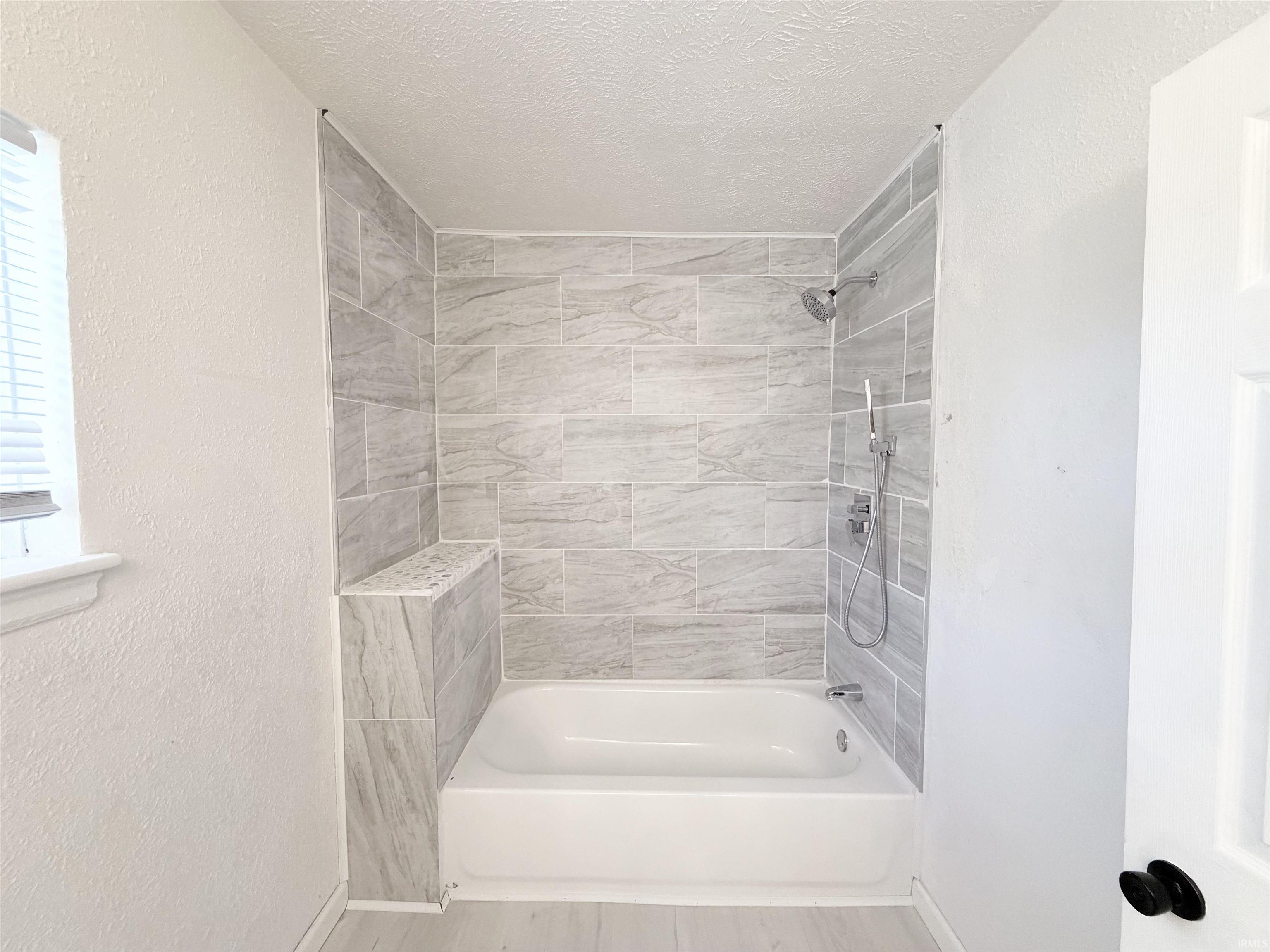 Bathtub and shower combination featuring extensive light-toned tile surround