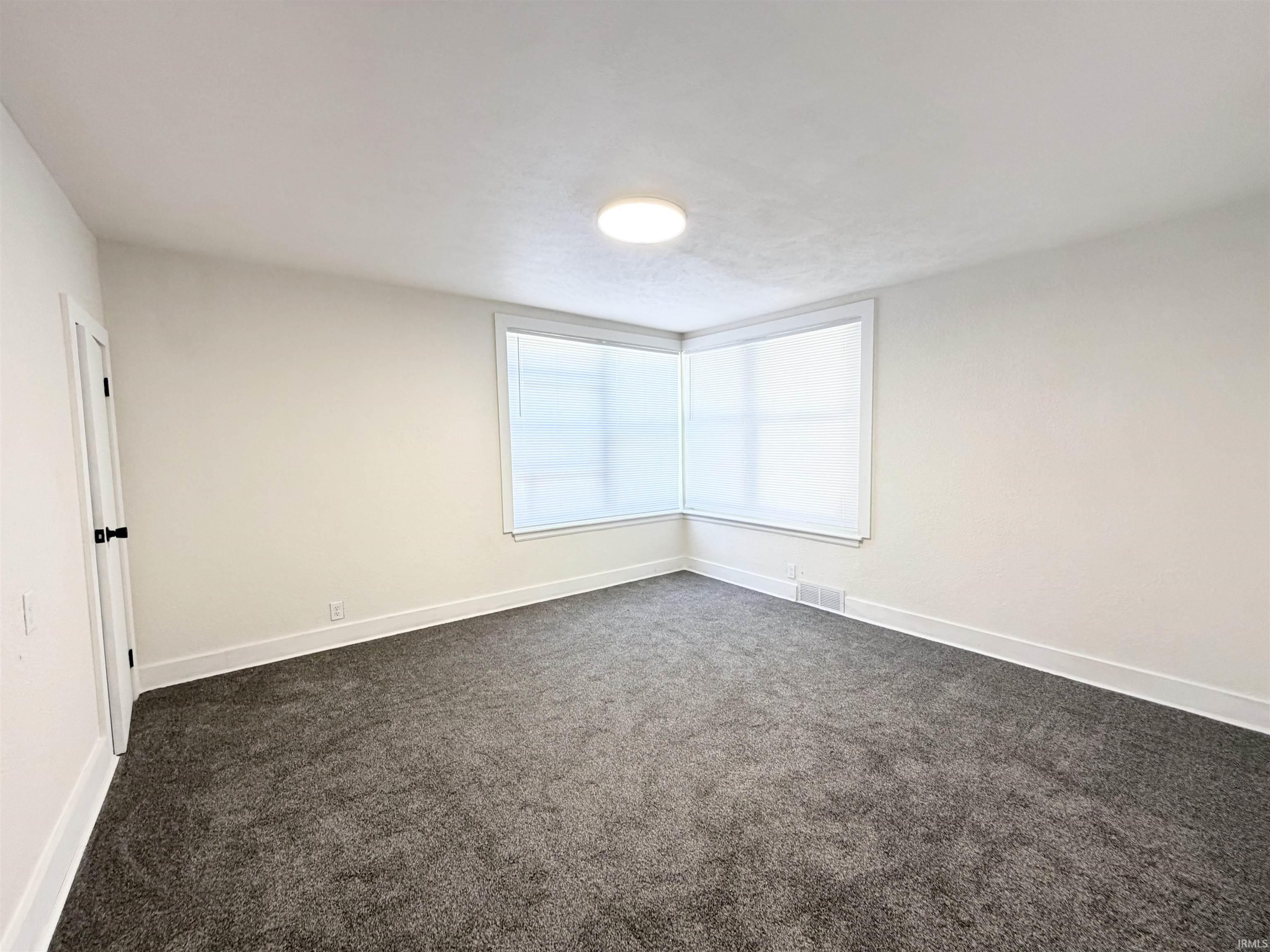 Room featuring neutral-toned carpeting, white walls, and a corner window arrangement with roller shades