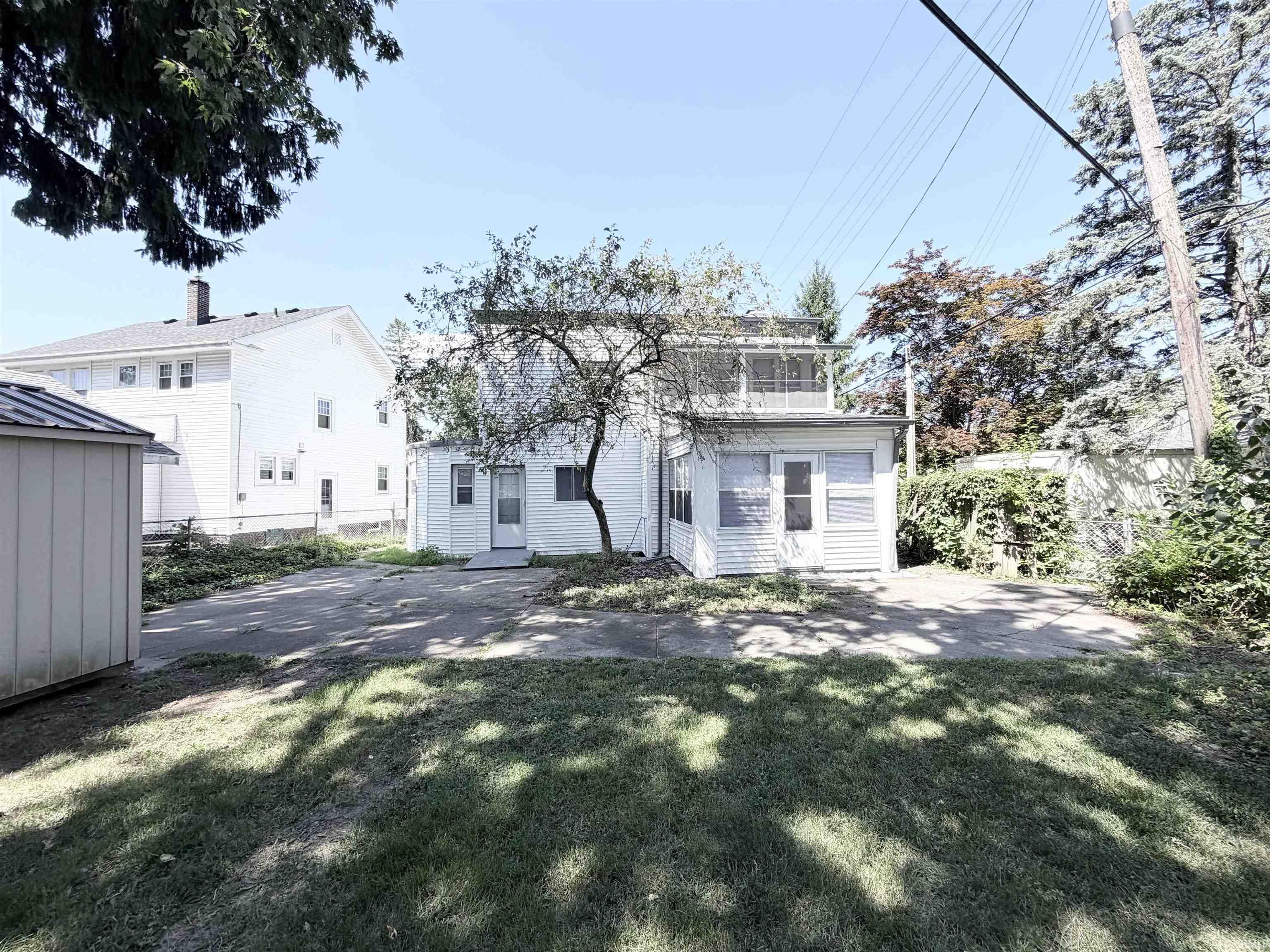 Rear exterior featuring a screened porch, upper-level enclosed balcony, and a paved patio area