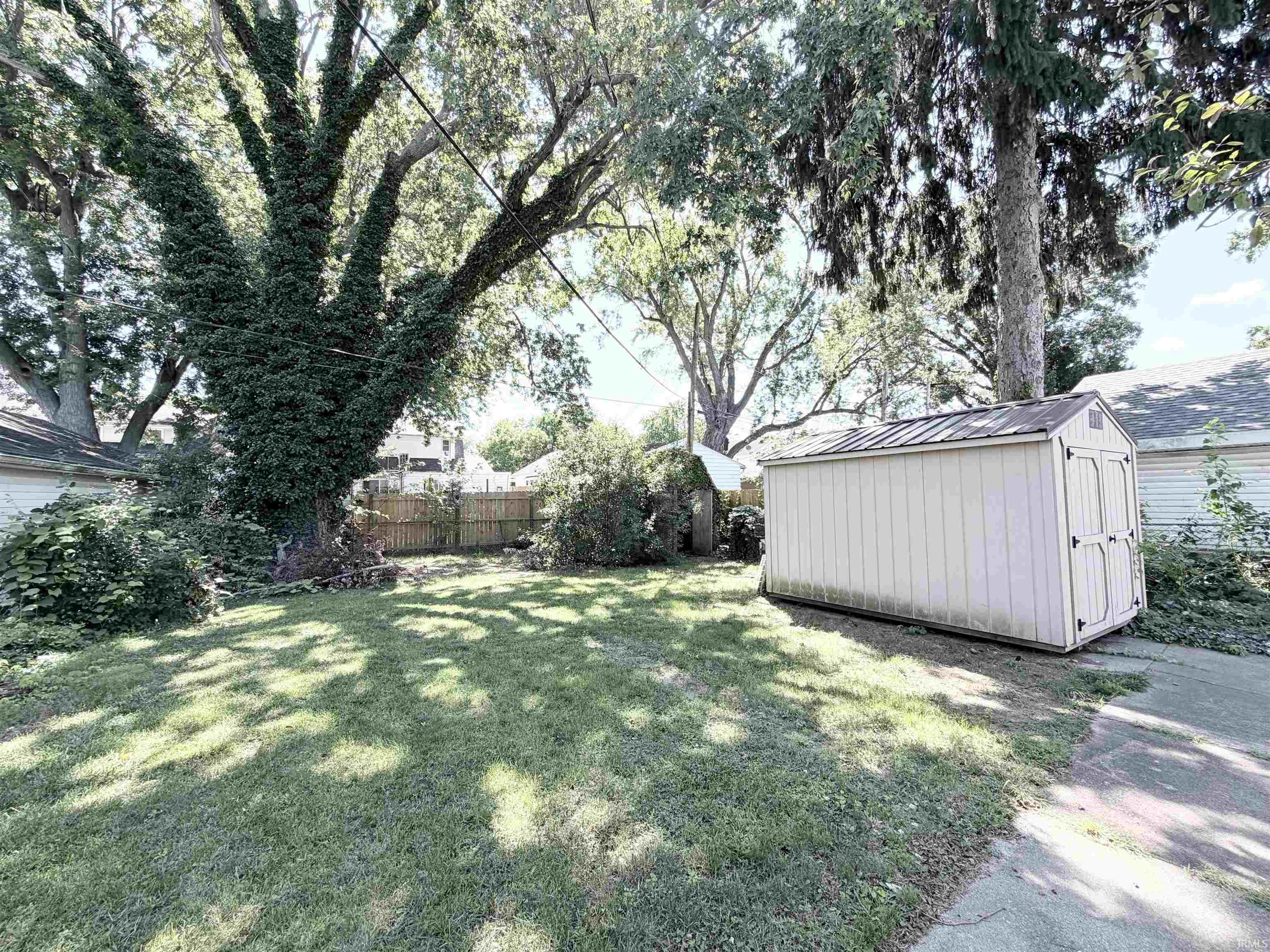 Spacious backyard featuring a manicured lawn, established shade trees, and a functional storage shed