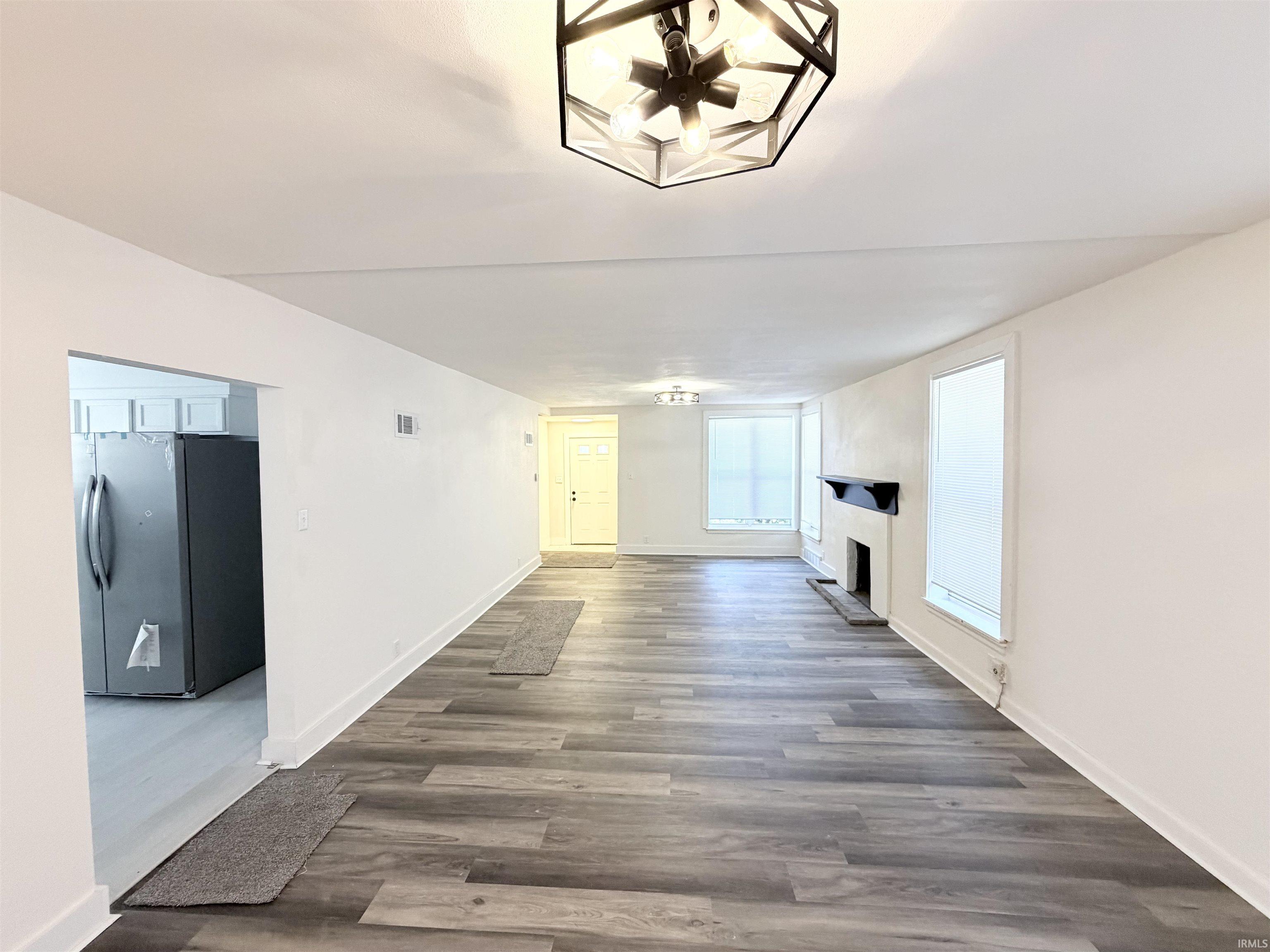 Spacious living area featuring wood-finish flooring, a decorative fireplace with a dark mantel, and multiple windows providing natural light