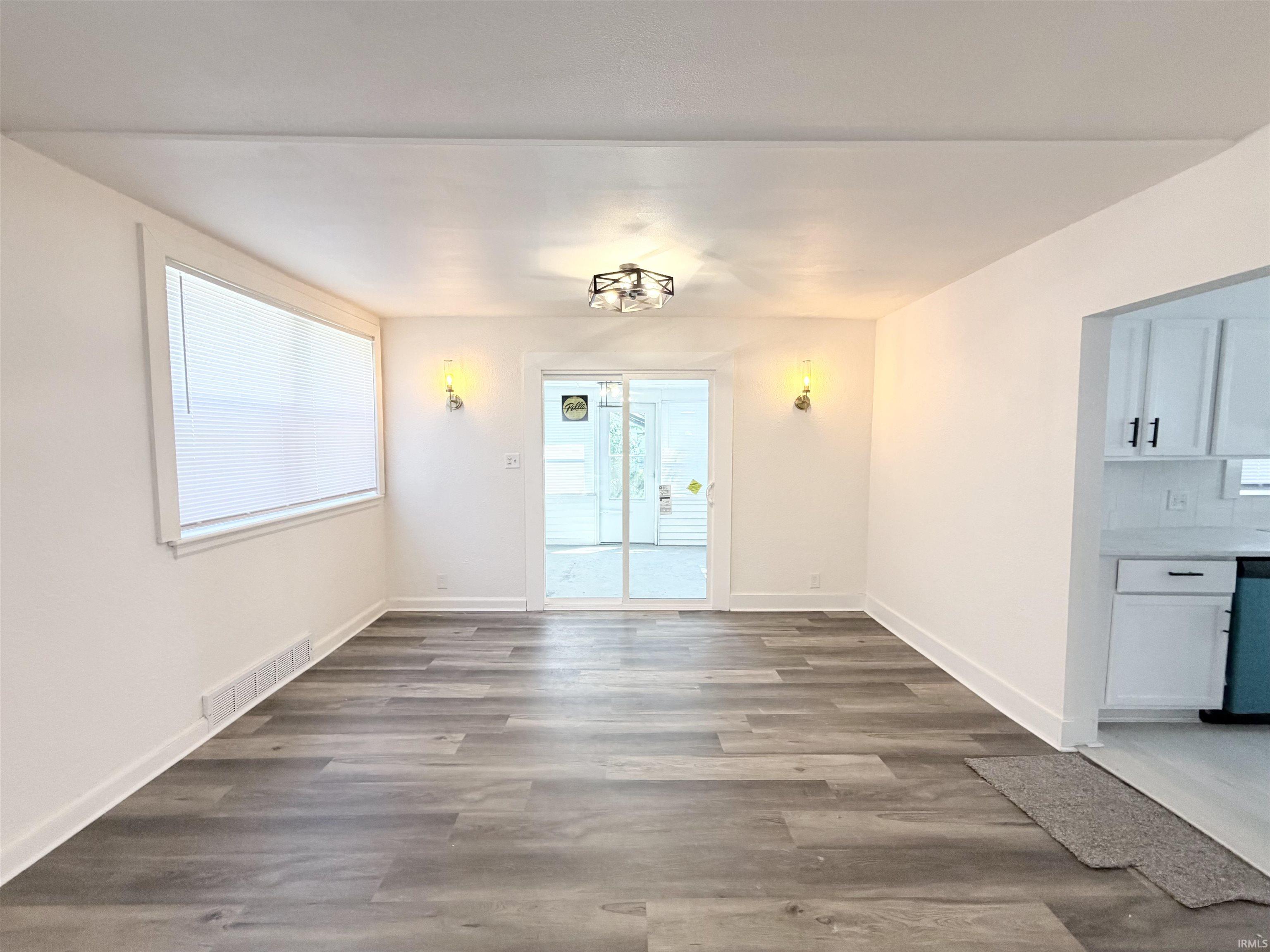 Spacious room featuring wood-finish flooring, white baseboards, and a large window with white blinds