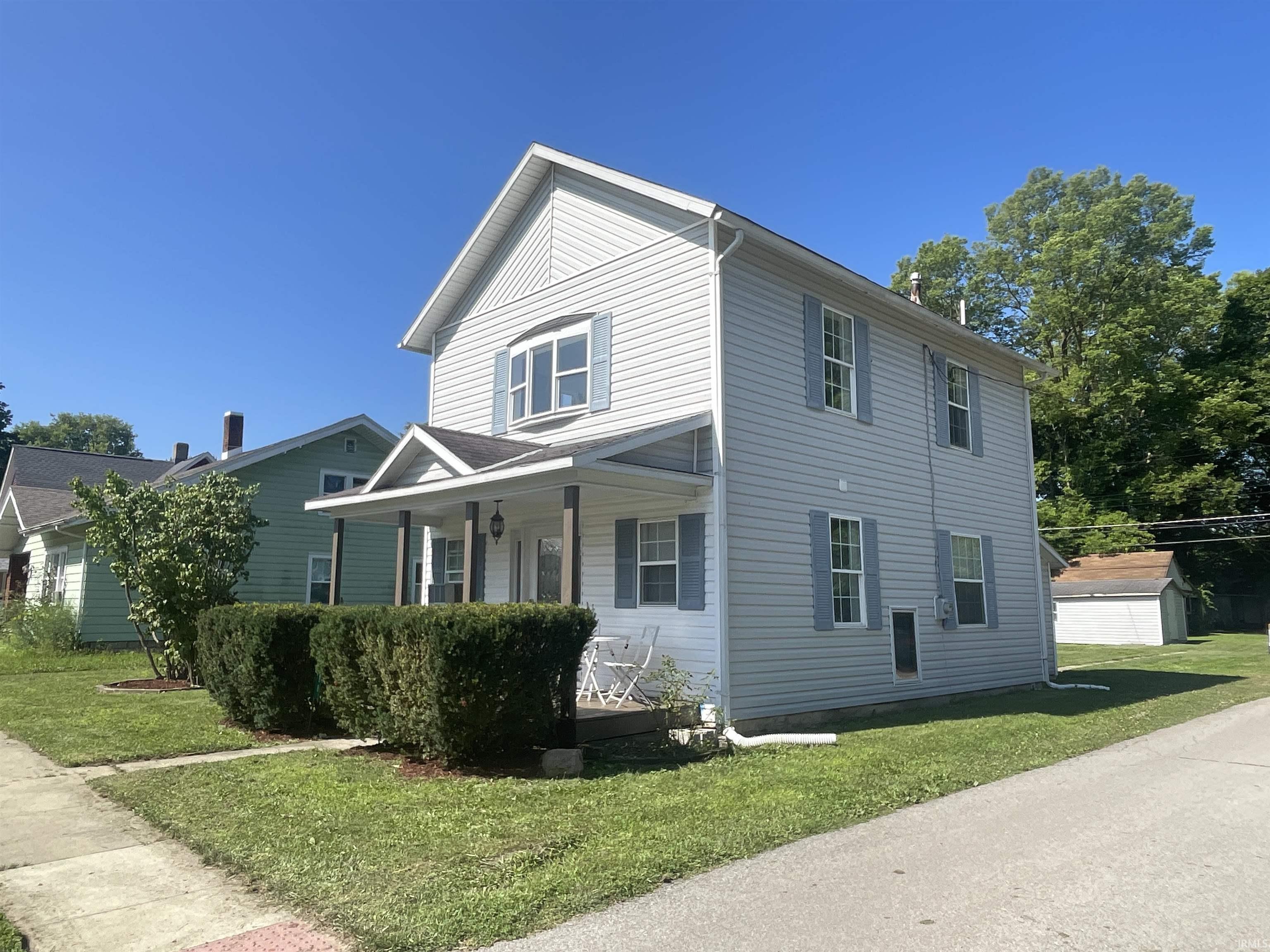 Two-story residence featuring light gray siding, a covered front porch with white columns, and blue window shutters