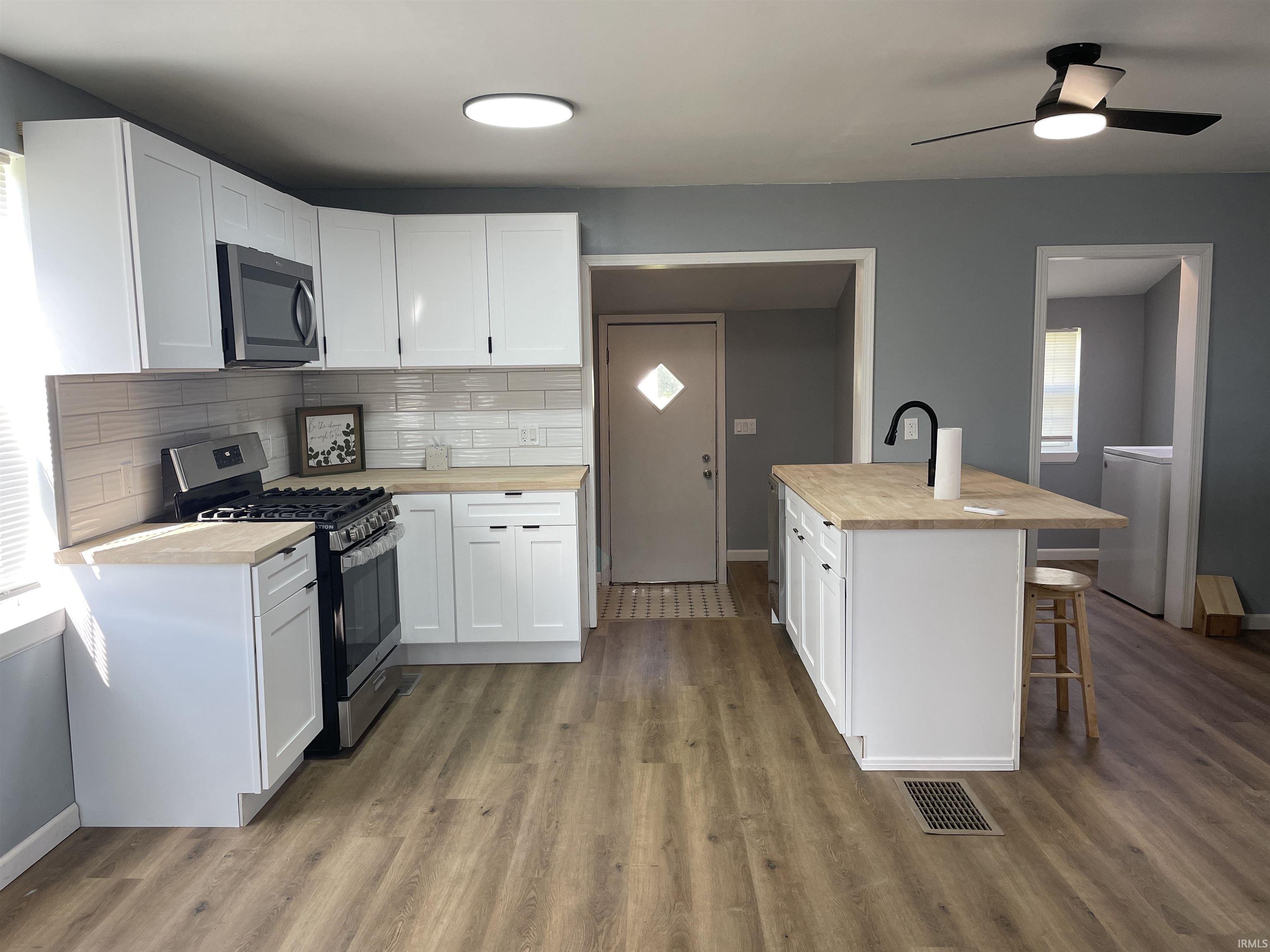 Kitchen featuring white cabinetry, light wood-finish countertops, stainless steel appliances, and wood-finish flooring