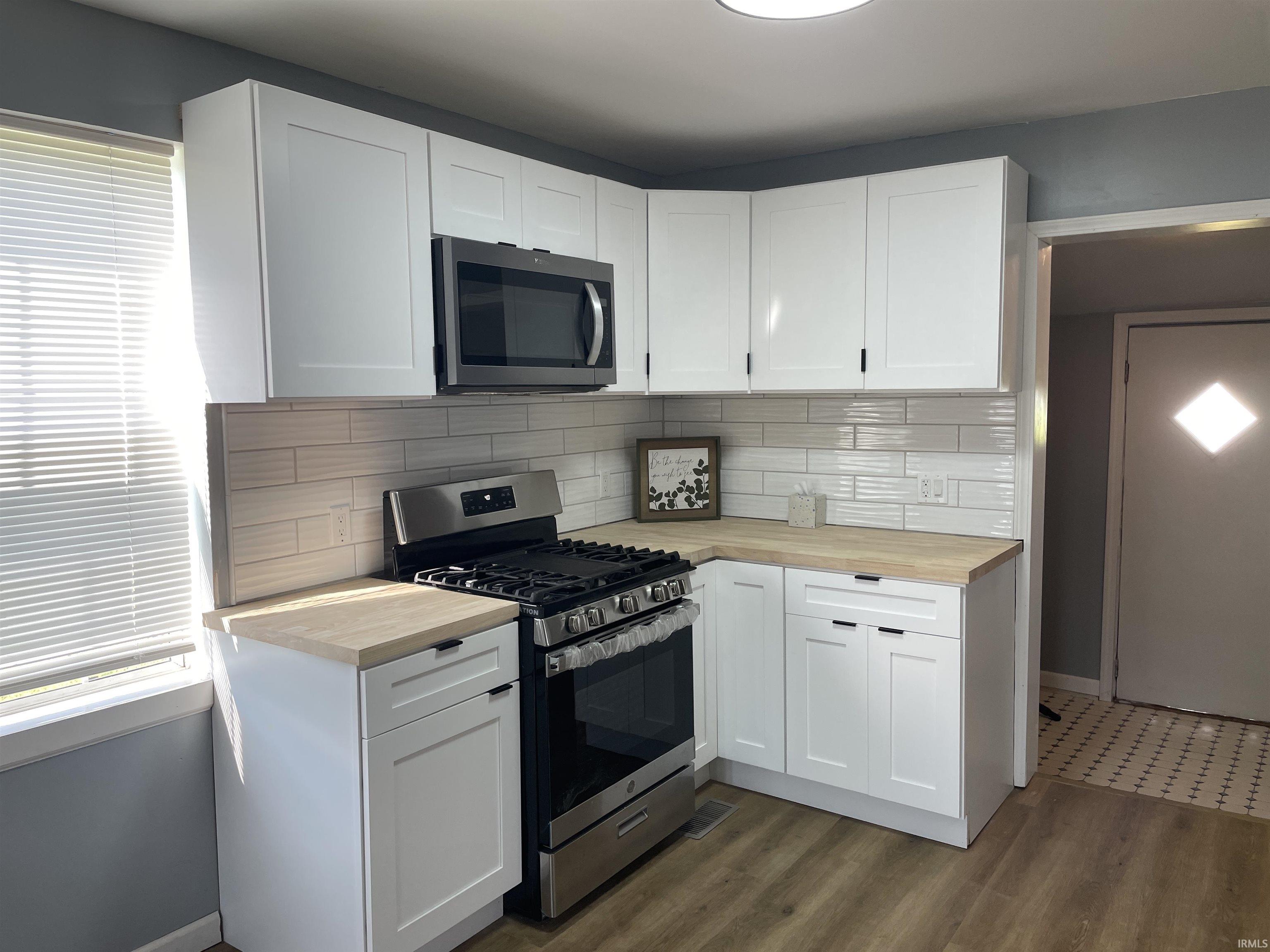 White shaker-style cabinetry, wood-finish countertops, stainless steel appliances, subway tile backsplash, and wood-finish flooring