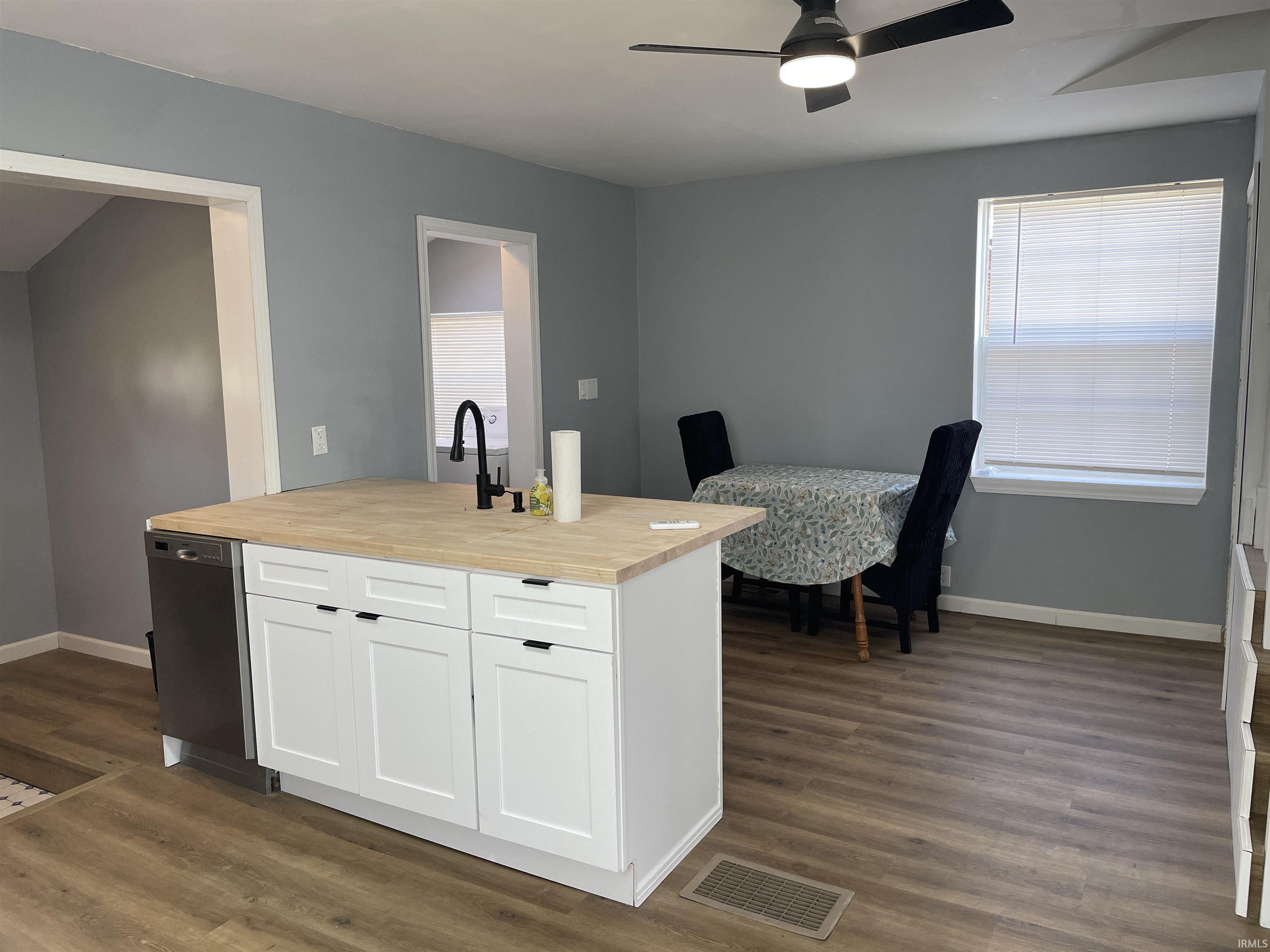 Kitchen island with wood-finish countertop, white cabinetry, and stainless steel dishwasher