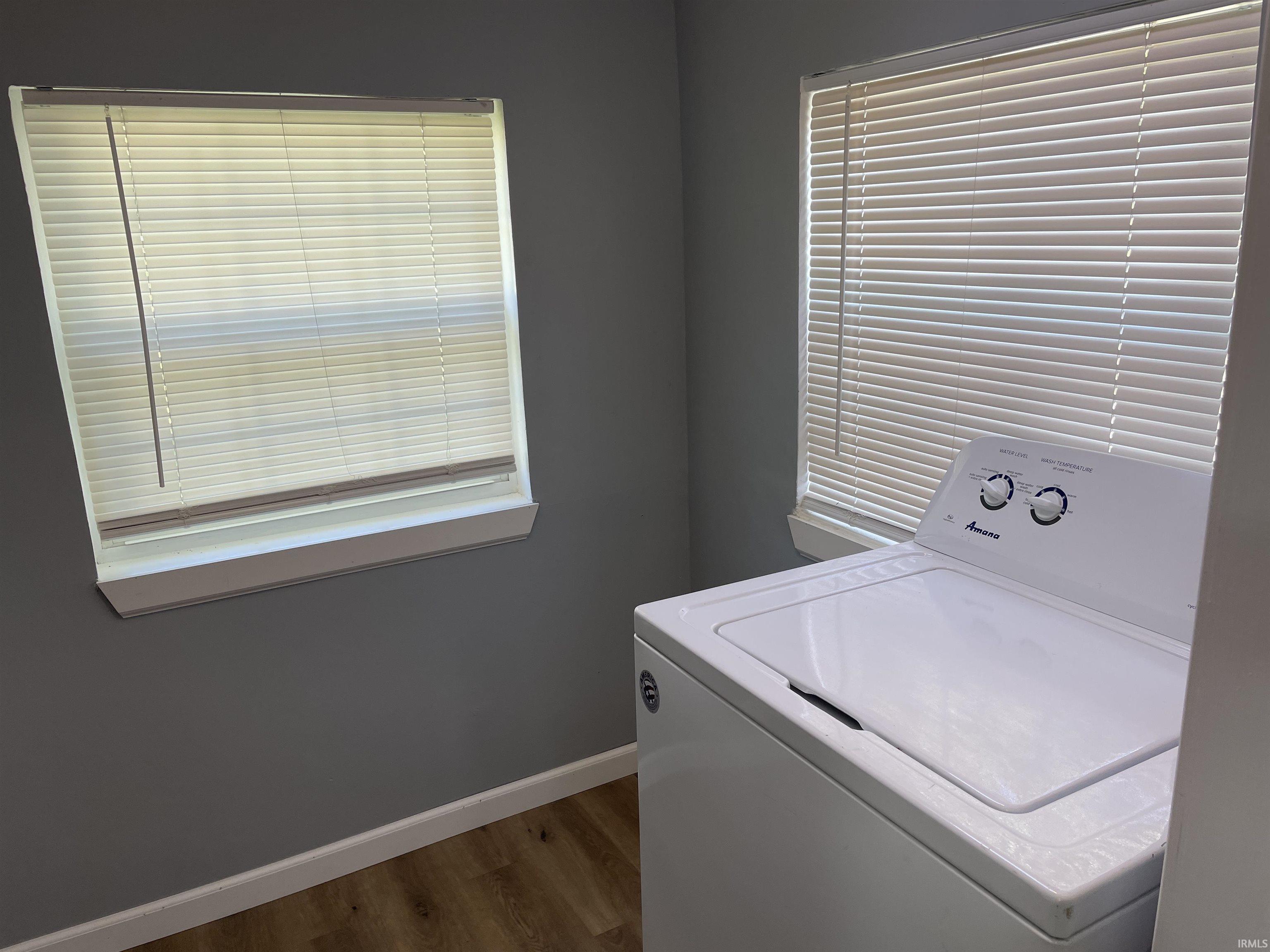 Two windows with white blinds, wood-finish flooring, and gray painted walls