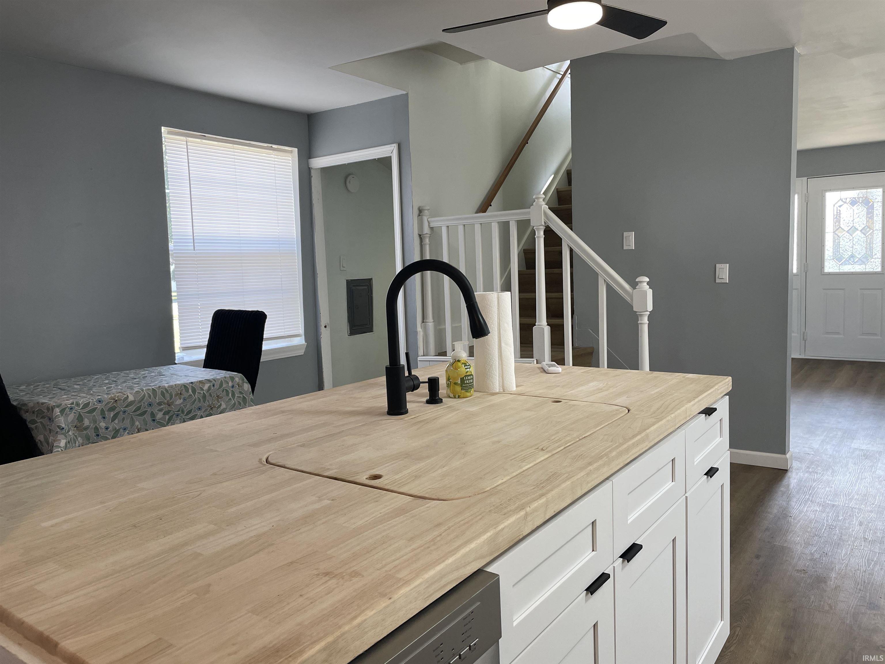 Kitchen island with wood-finish countertop, black gooseneck faucet, and white cabinetry with black hardware