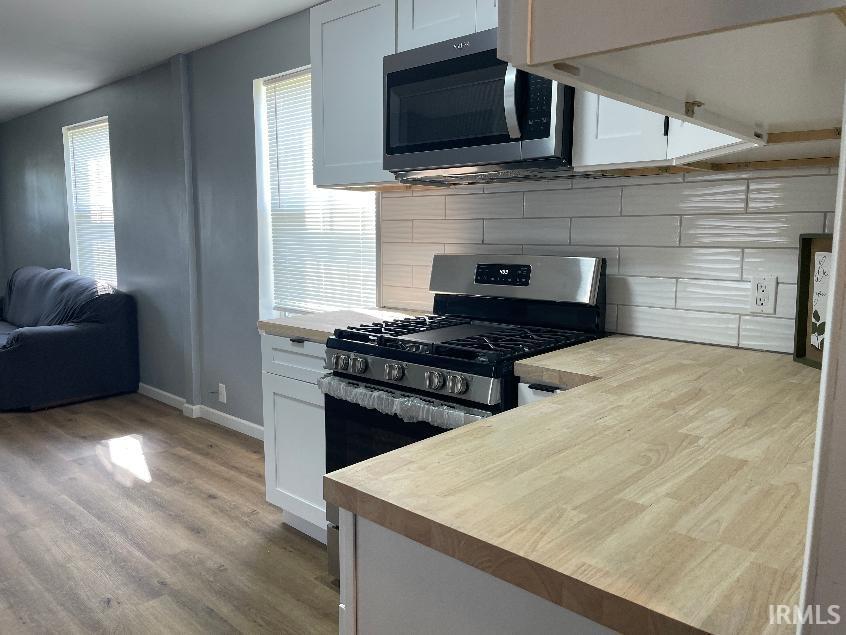 Modern kitchen featuring stainless steel gas range with multiple burners, integrated microwave hood, light wood-finish countertops, white cabinetry with ample storage, and white subway tile backsplash