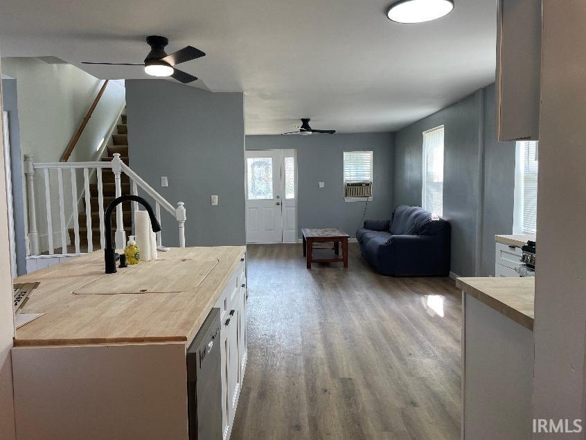 Open-concept kitchen and living area featuring wood-finish flooring throughout, white cabinetry with wood countertops, recessed and ceiling fan lighting, and gray wall finishes