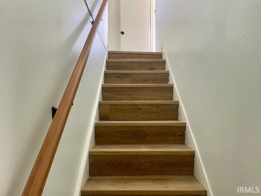 Staircase featuring wood-finish treads and risers, a light wood handrail, and white painted walls