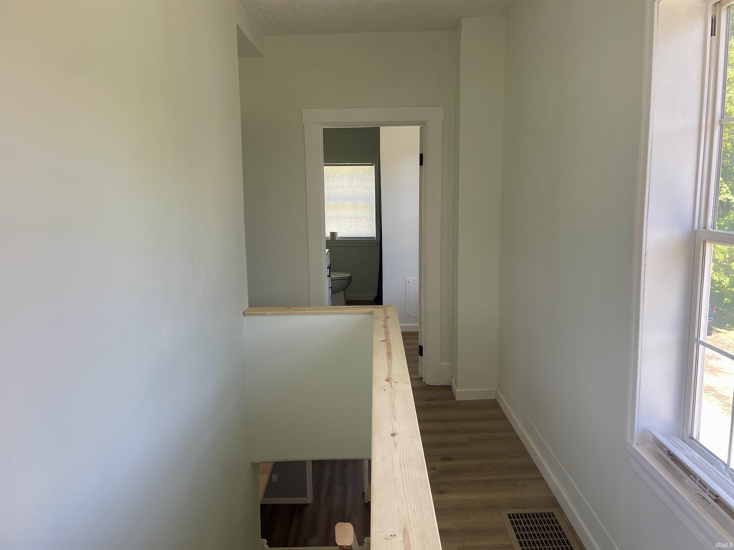 Second-level hallway featuring wood-finish flooring, light-colored wall paint, white trim, and natural light from a window