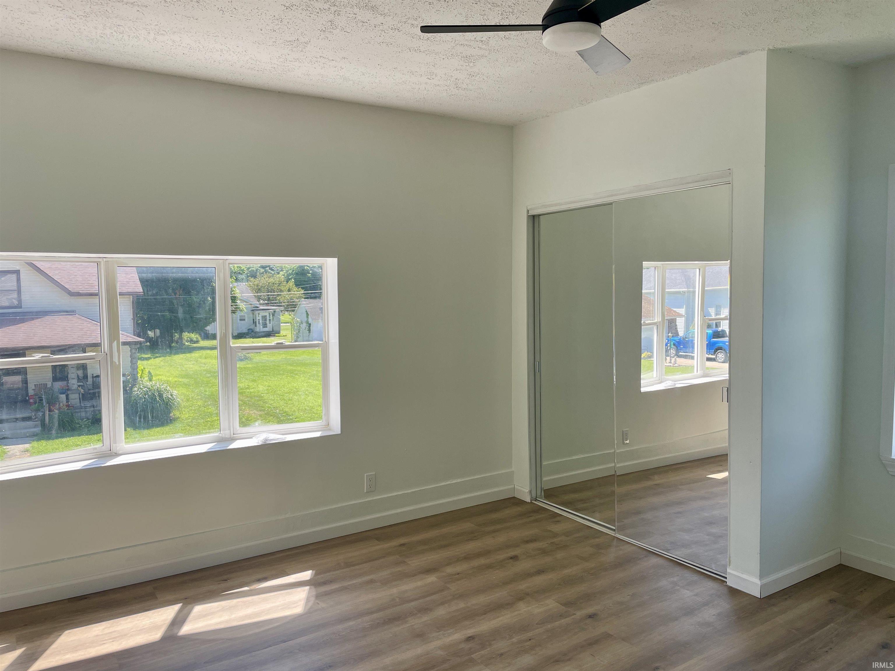 Bright interior featuring wood-finish flooring, white baseboards, a modern ceiling fan, and large windows