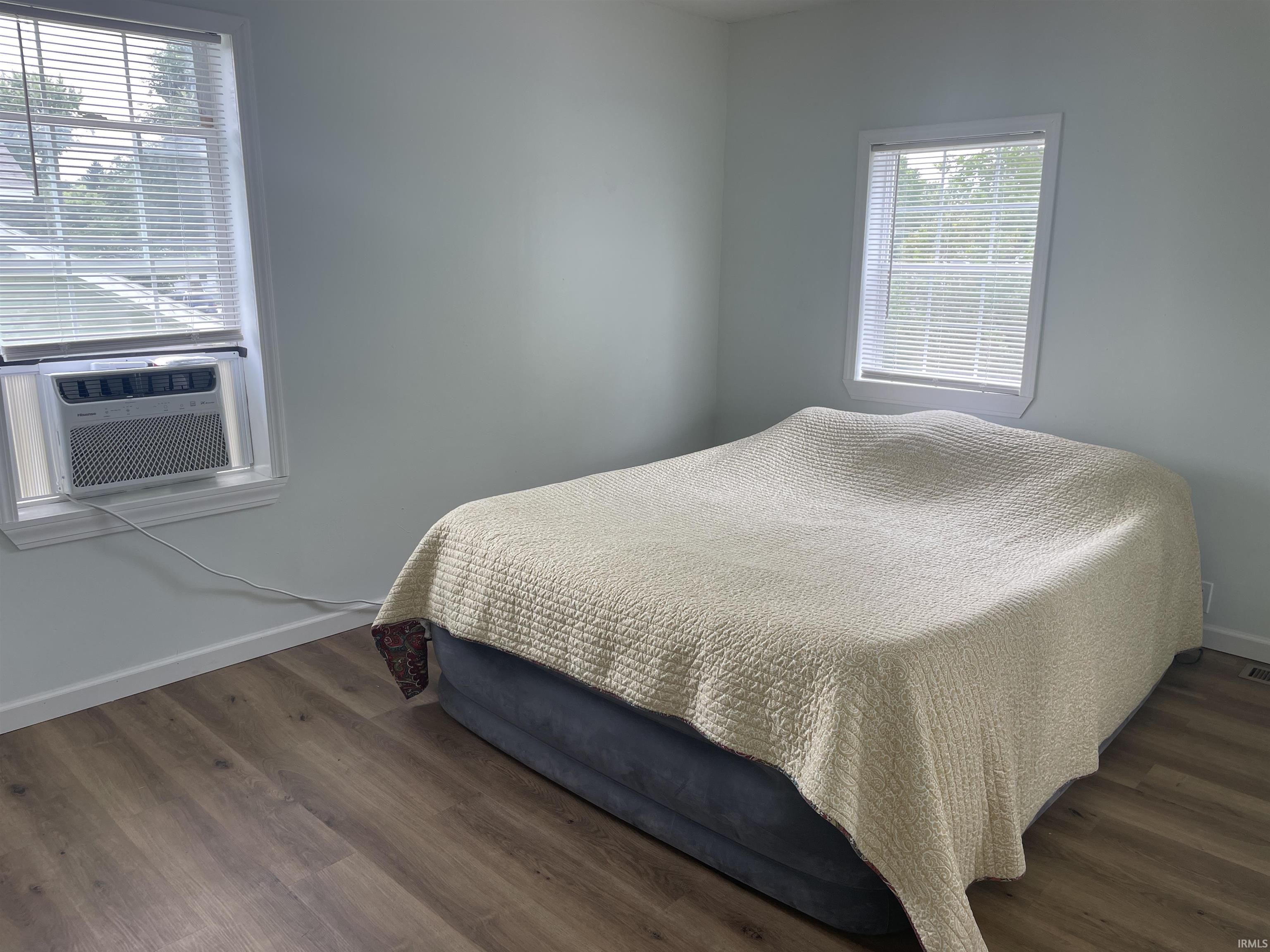 Room featuring wood-finish flooring, light-toned wall paint, and two windows with blinds
