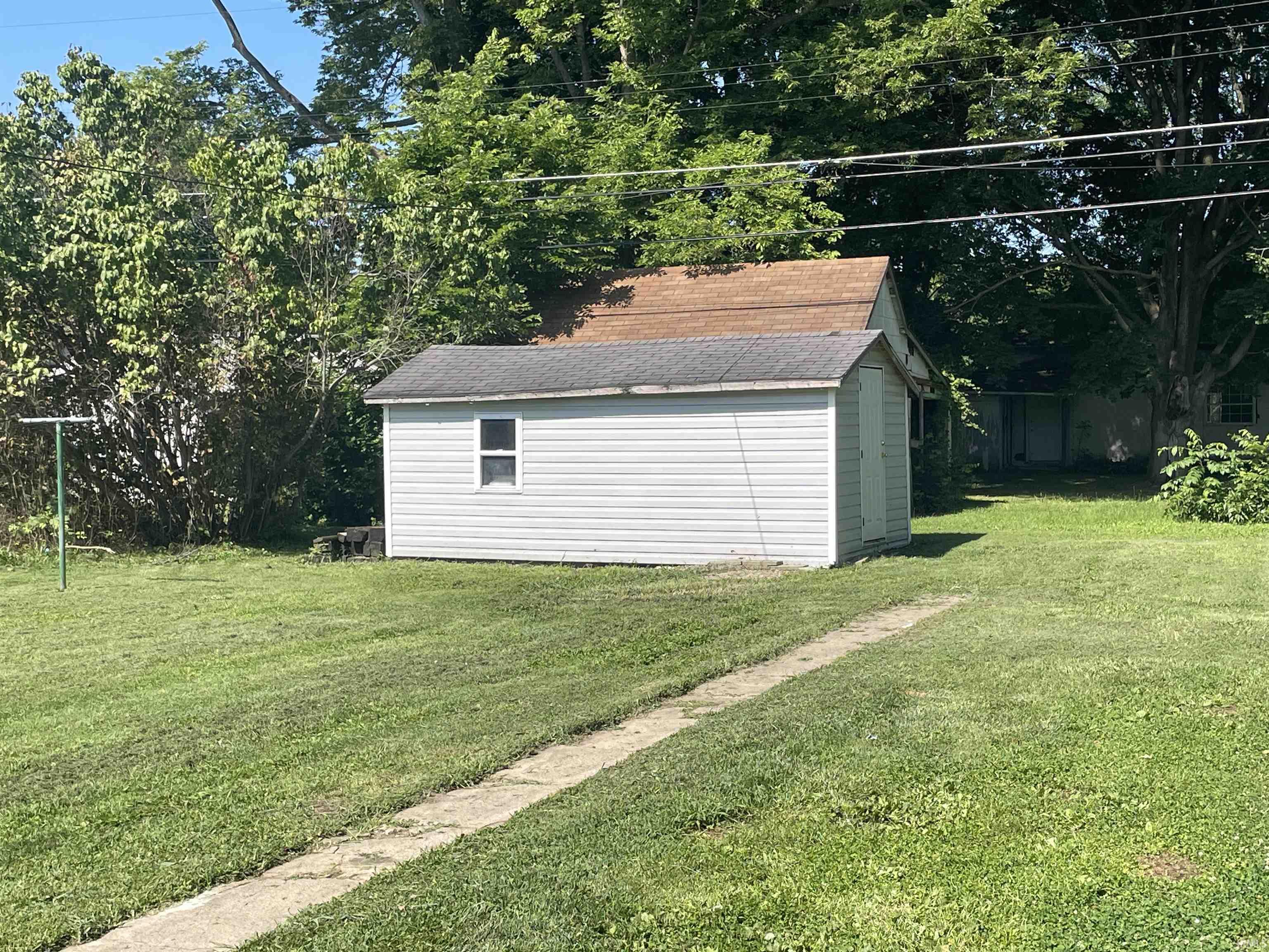 Detached storage shed with white siding and a single window, featuring a dark shingled roof