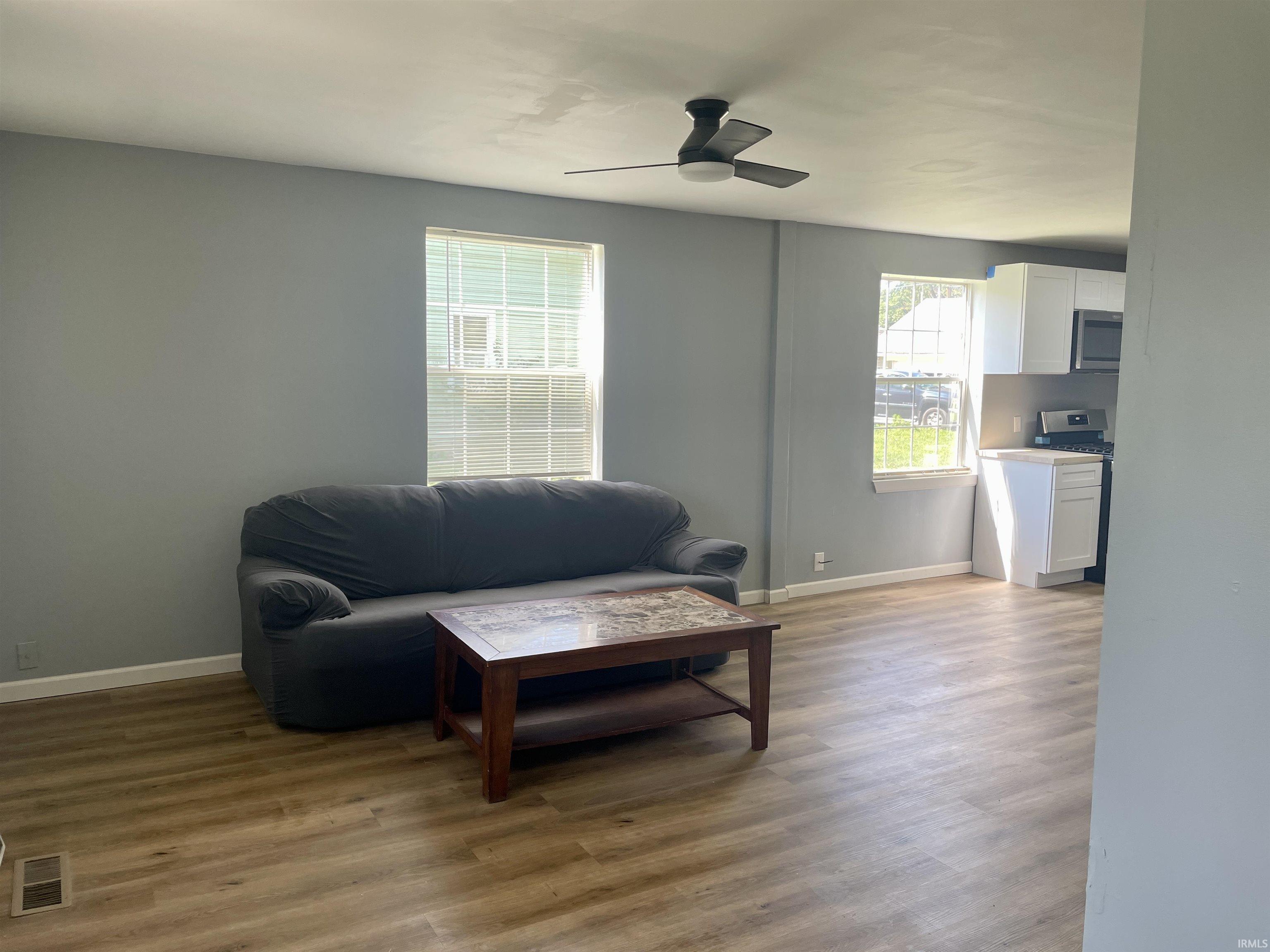 Open-concept living space featuring wood-finish flooring, a contemporary ceiling fan, and abundant natural light from multiple windows