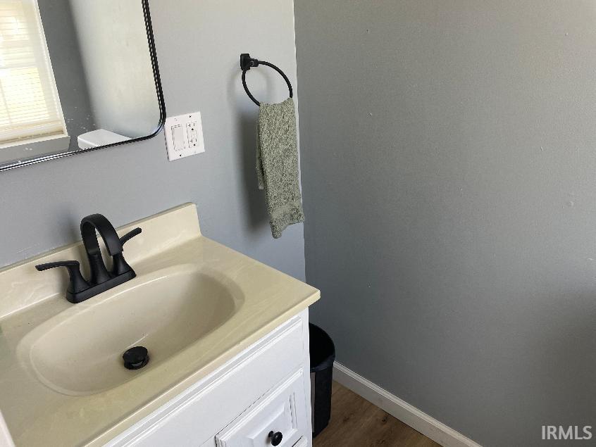 Vanity with a built-in basin and matte black faucet, framed mirror, and wood-finish flooring