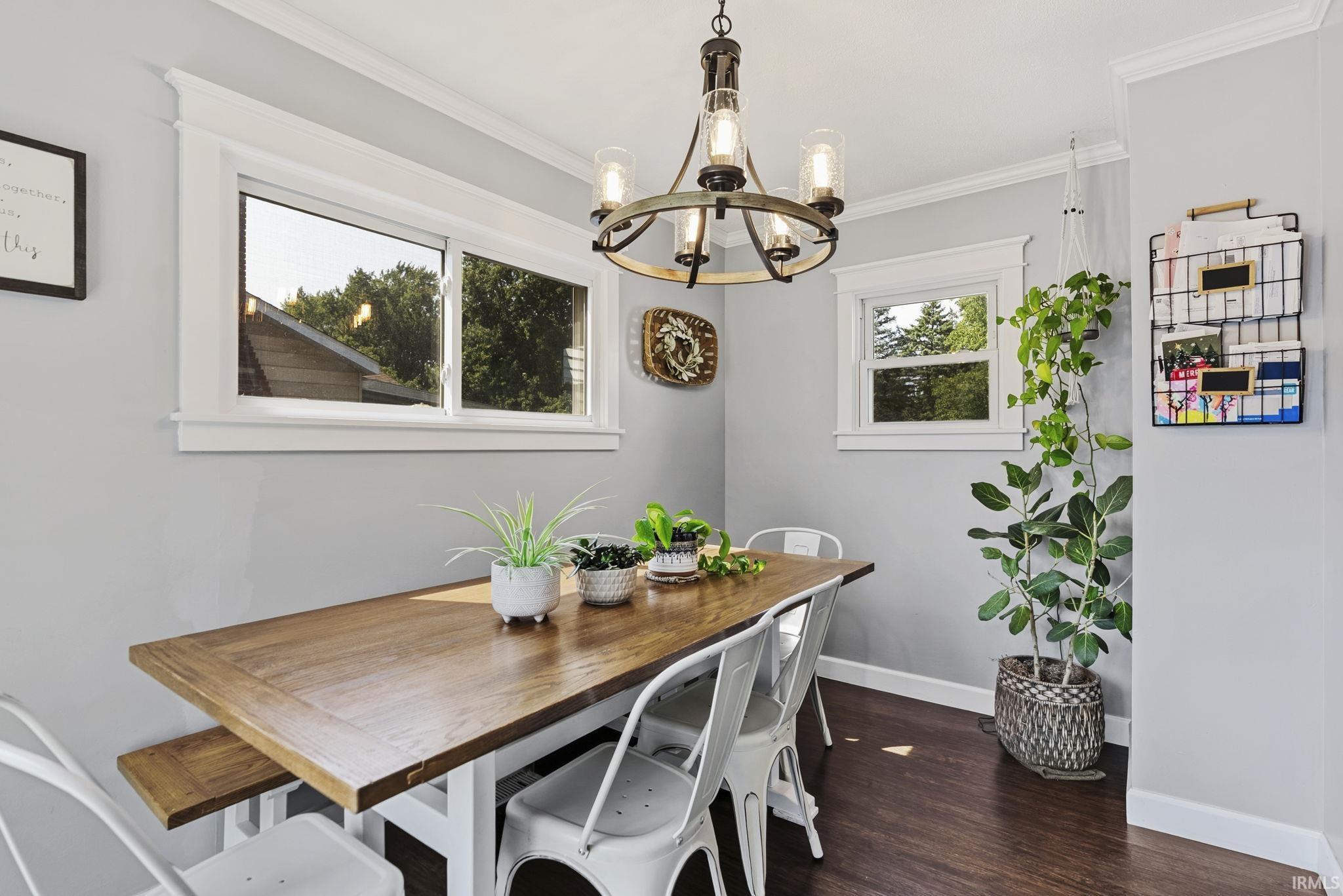 Dining area featuring a wood-finish table, multiple windows, a pendant light fixture, crown molding, and dark wood-finish flooring