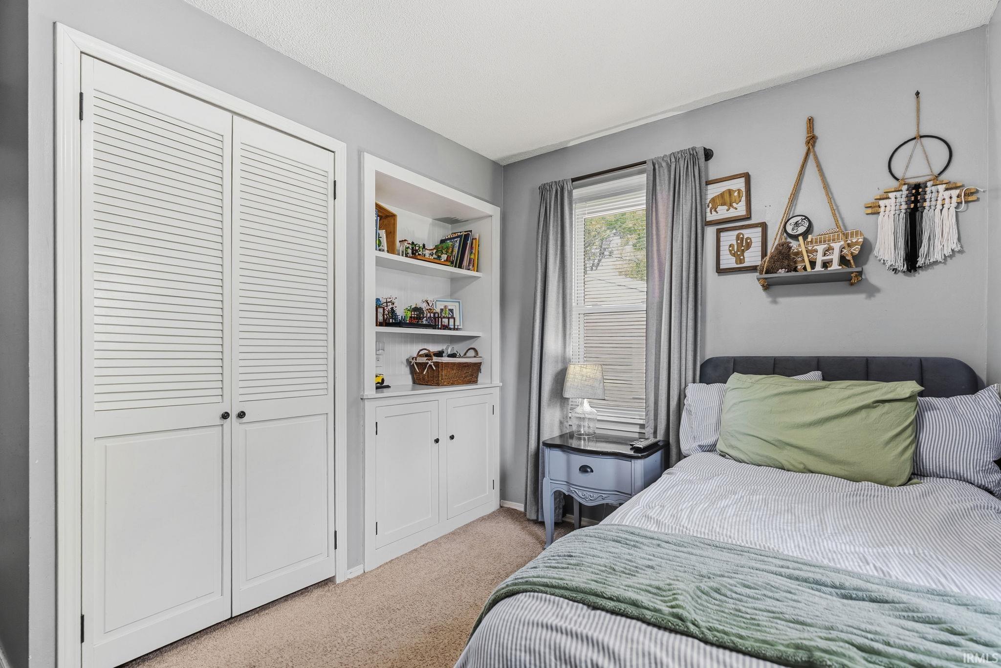 Built-in cabinetry featuring open shelving and lower cabinets, louvered bi-fold closet doors, a single window with blinds, and light gray wall paint