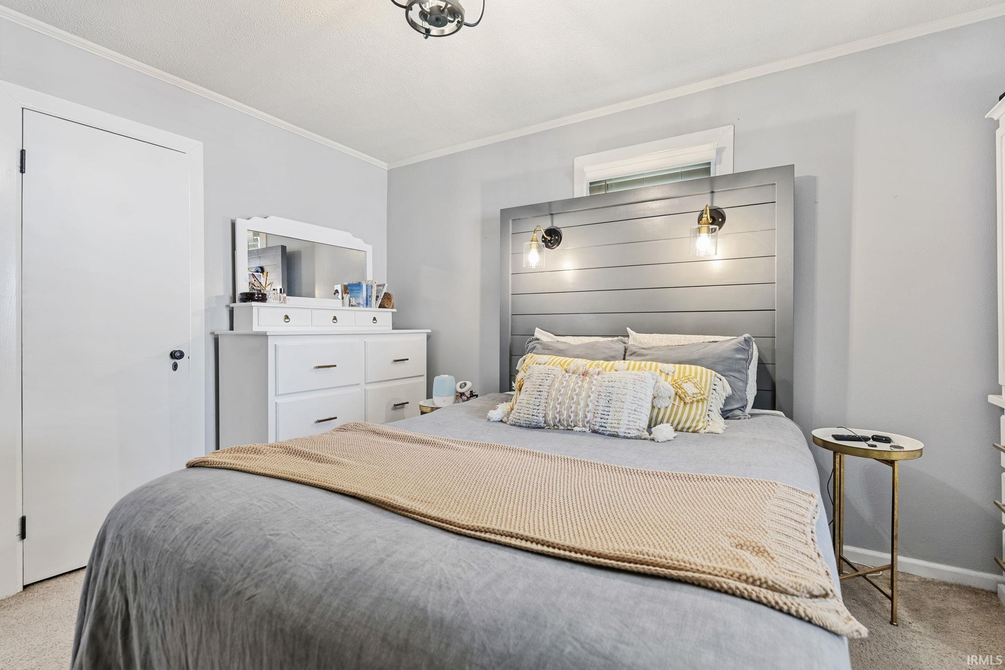 Neutral-toned bedroom featuring a light gray wall color, carpet flooring, a built-in headboard with integrated sconce lighting, and white trim