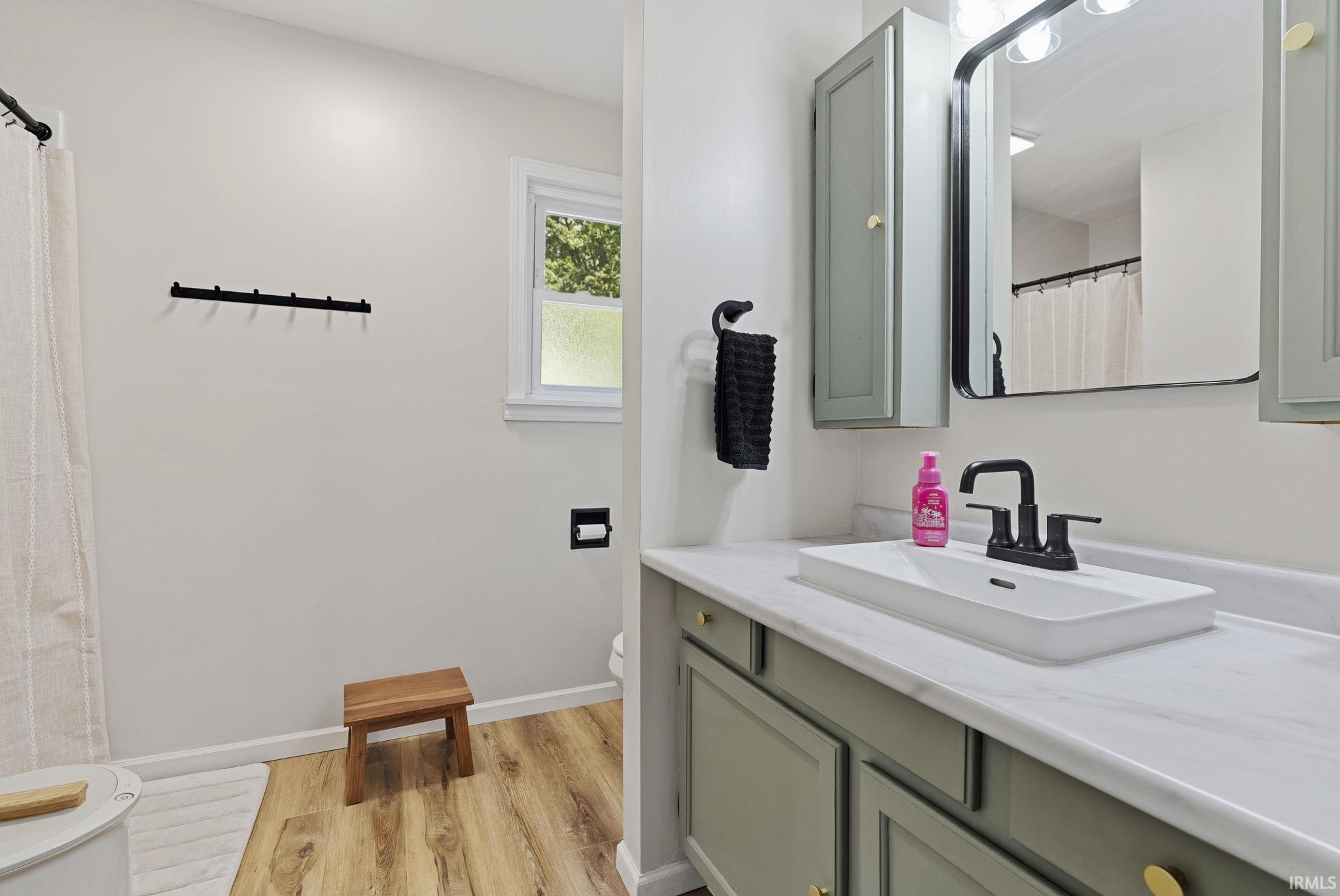 Bathroom featuring a modern vanity with light green cabinetry, gold-tone hardware, a white rectangular vessel sink, and a black-finish faucet