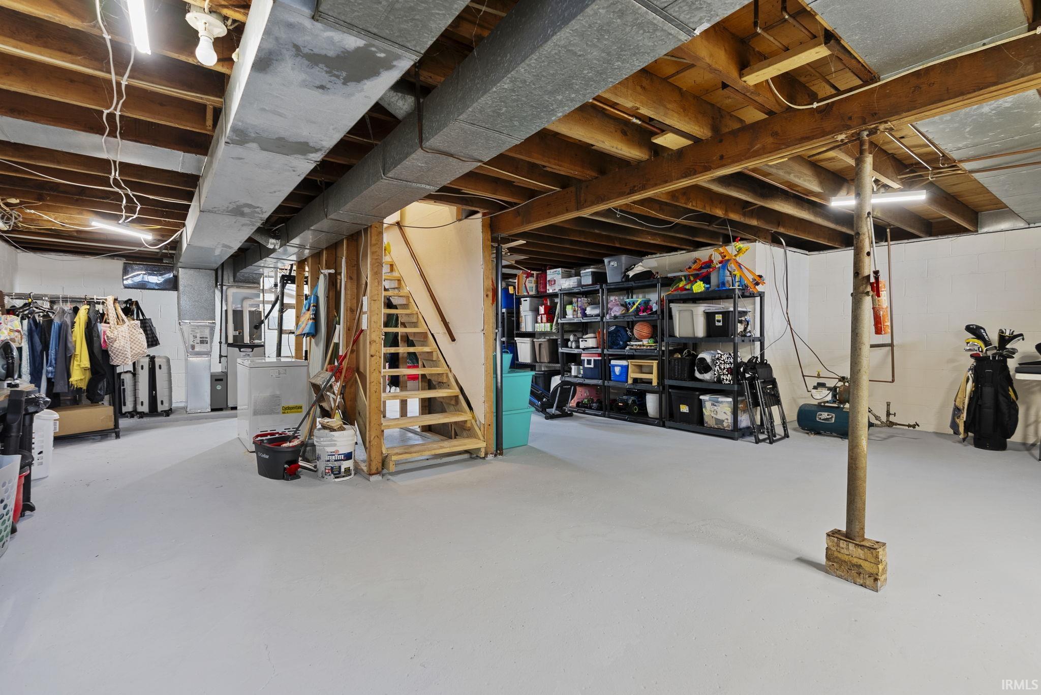 Expansive unfinished basement featuring concrete flooring, exposed wood beam ceiling, exposed ductwork, and an unfinished wood staircase