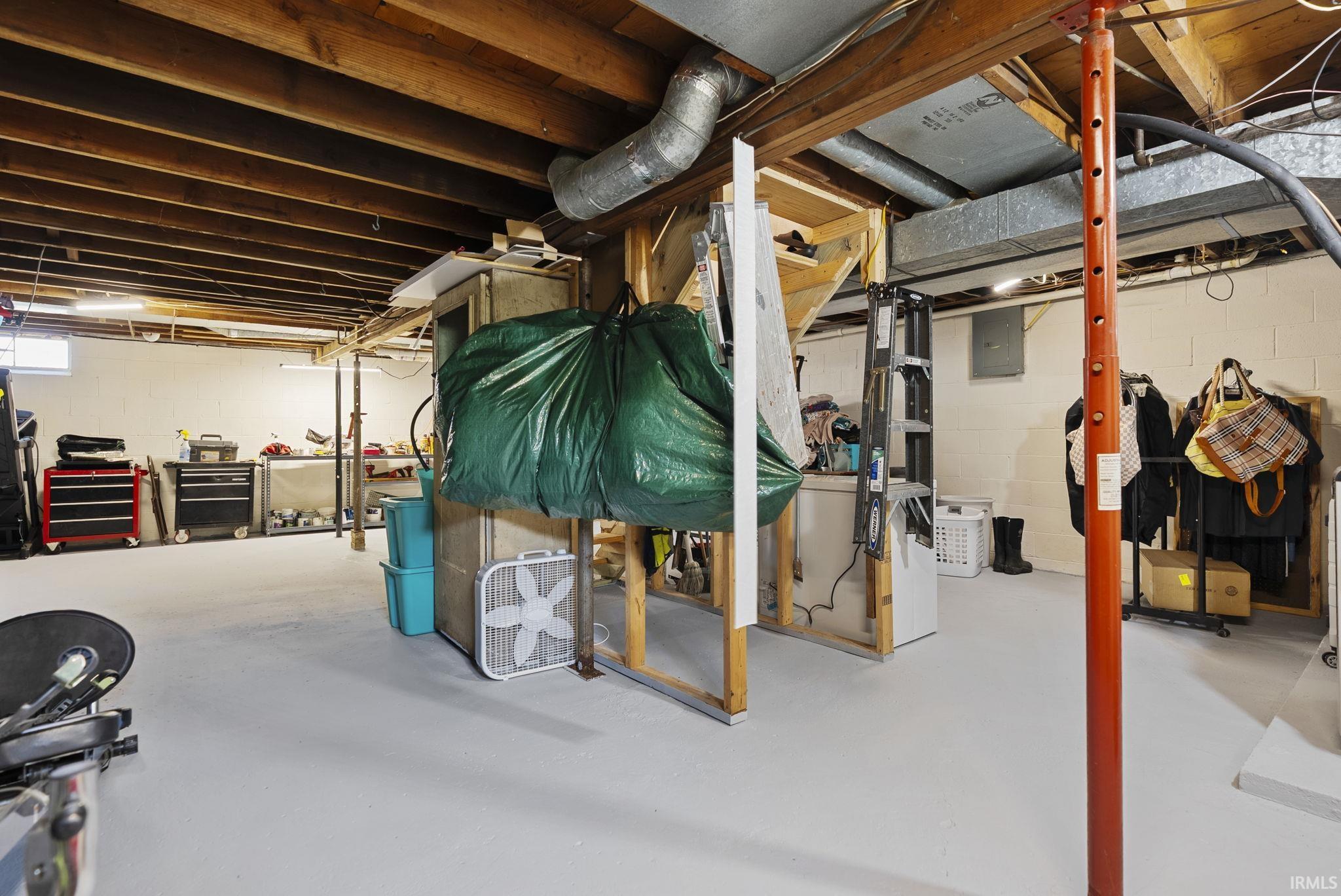Basement space featuring exposed wood joists, painted concrete flooring, and visible ductwork