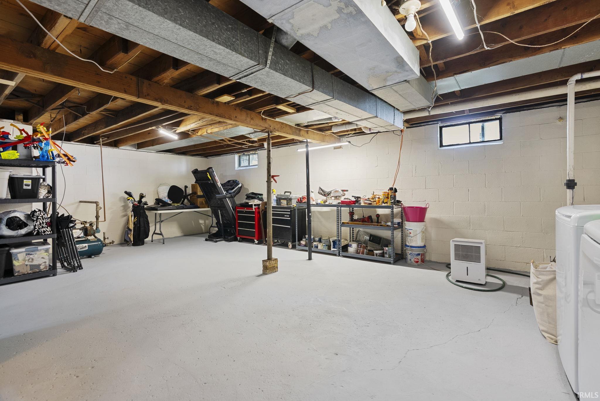Expansive unfinished basement featuring painted concrete block walls, exposed wood ceiling joists, and concrete flooring