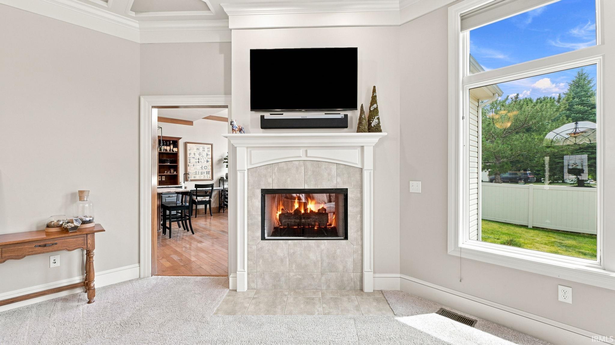 Built-in fireplace with a tiled surround and mantel, large window overlooking a fenced yard, recessed ceiling detail, and carpeted flooring