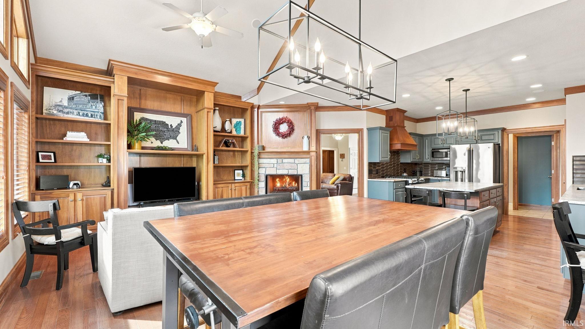 Open-concept living space featuring wood-finish flooring, a built-in media center with shelving, a stone fireplace, a kitchen island, and a range hood