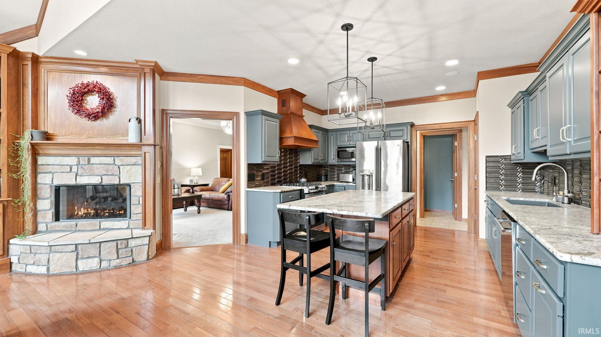 Spacious kitchen featuring hardwood flooring, stone fireplace, granite countertops, stainless steel appliances, and custom cabinetry