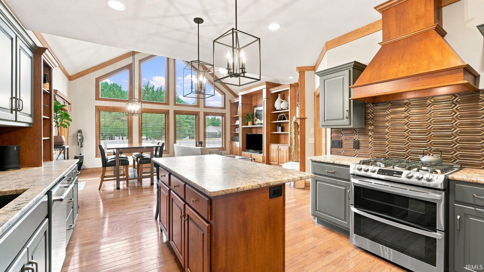 Open-concept kitchen featuring an island with stone-finish countertops, wood-finish flooring, a stainless steel gas range, and an integrated wood-finish range hood