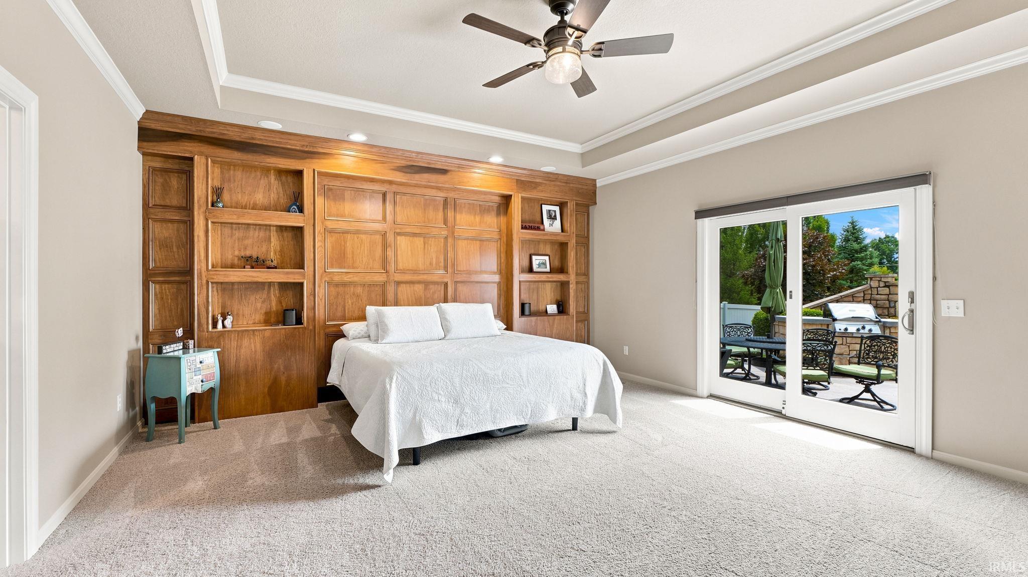 Spacious room featuring a custom wood-finish built-in shelving unit, tray ceiling, and ceiling fan